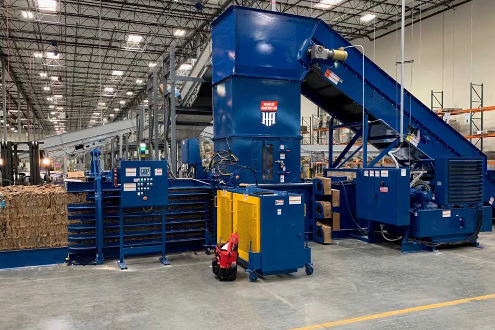 Industrial recycling machine with conveyor belt and baler in a large warehouse facility.