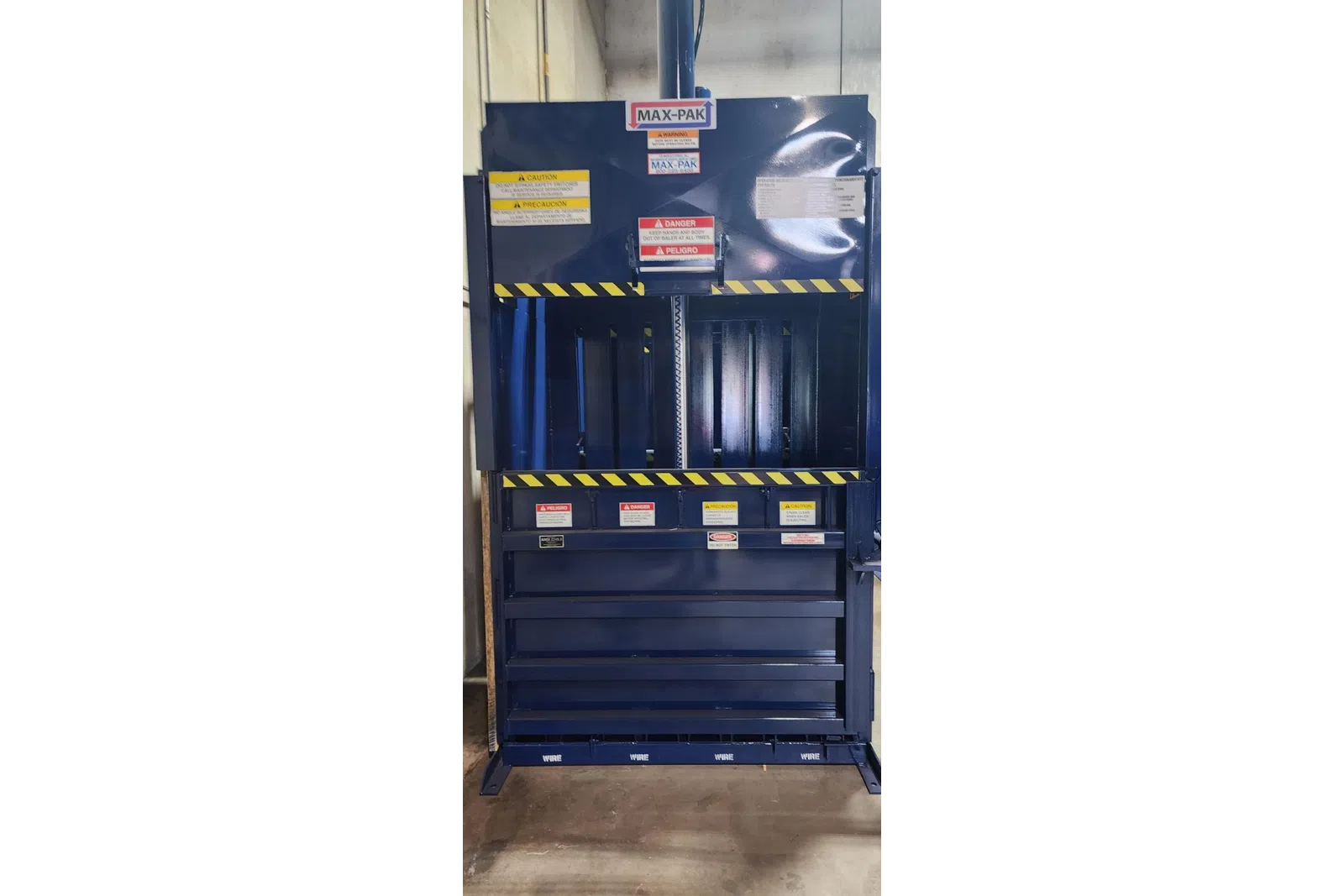 Blue Max-Pak industrial baler machine with multiple caution and danger warning labels in a warehouse setting