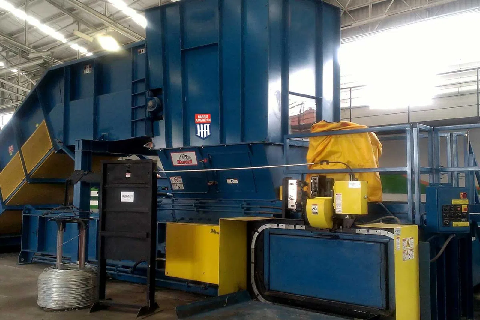 Large blue and yellow industrial machine inside a warehouse with metal coils and control panels.