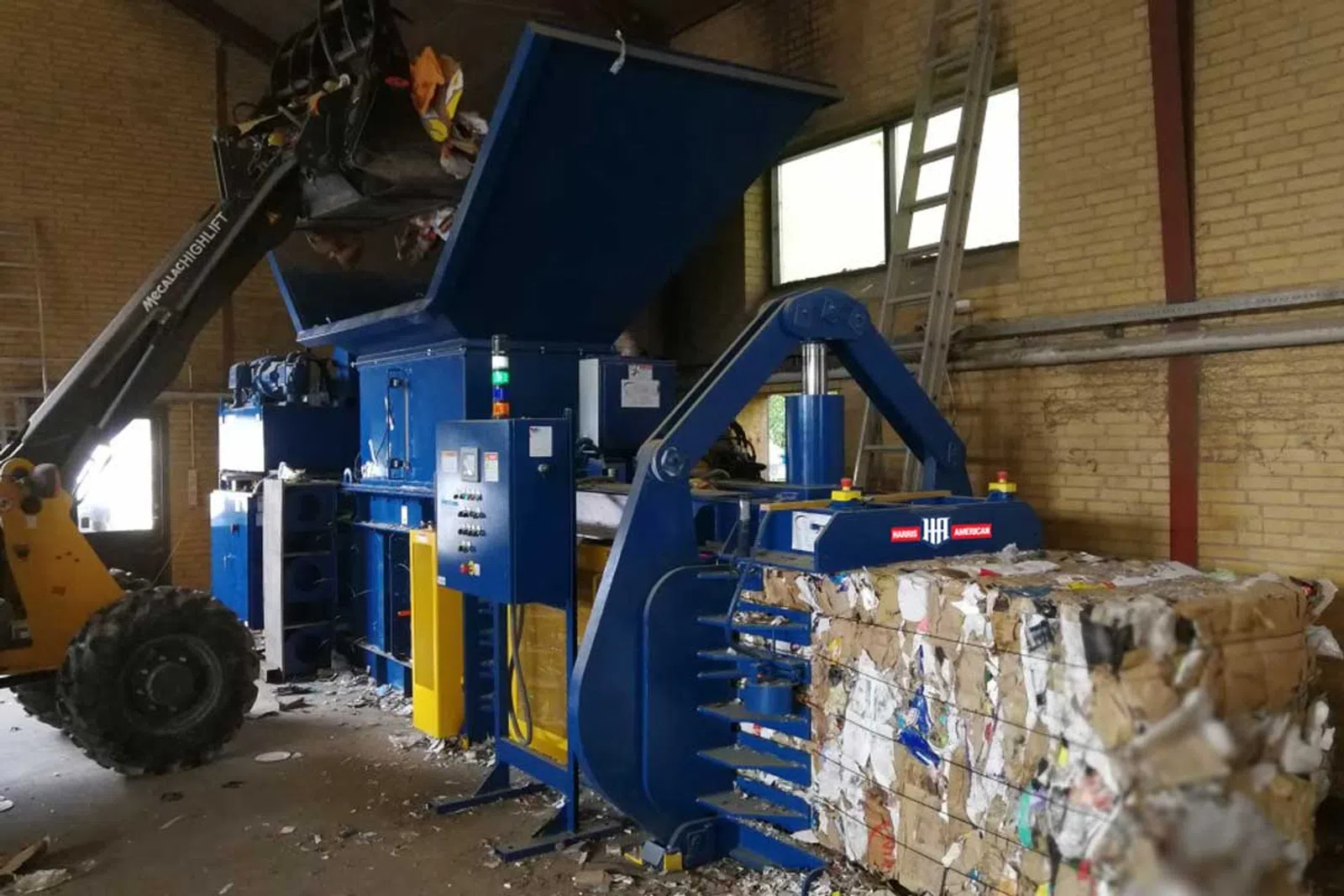 Industrial cardboard baler machine compressing recycled paper into compact bales inside warehouse.
