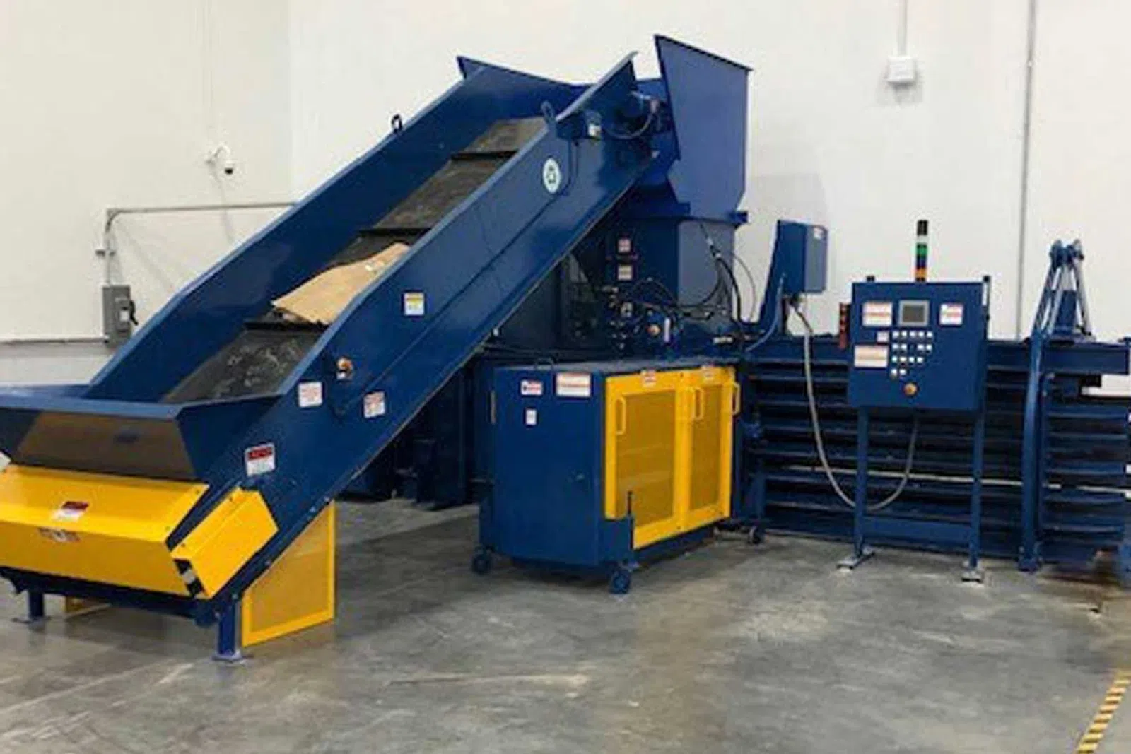 Industrial baler machine with conveyor belt and control panel in a factory setting