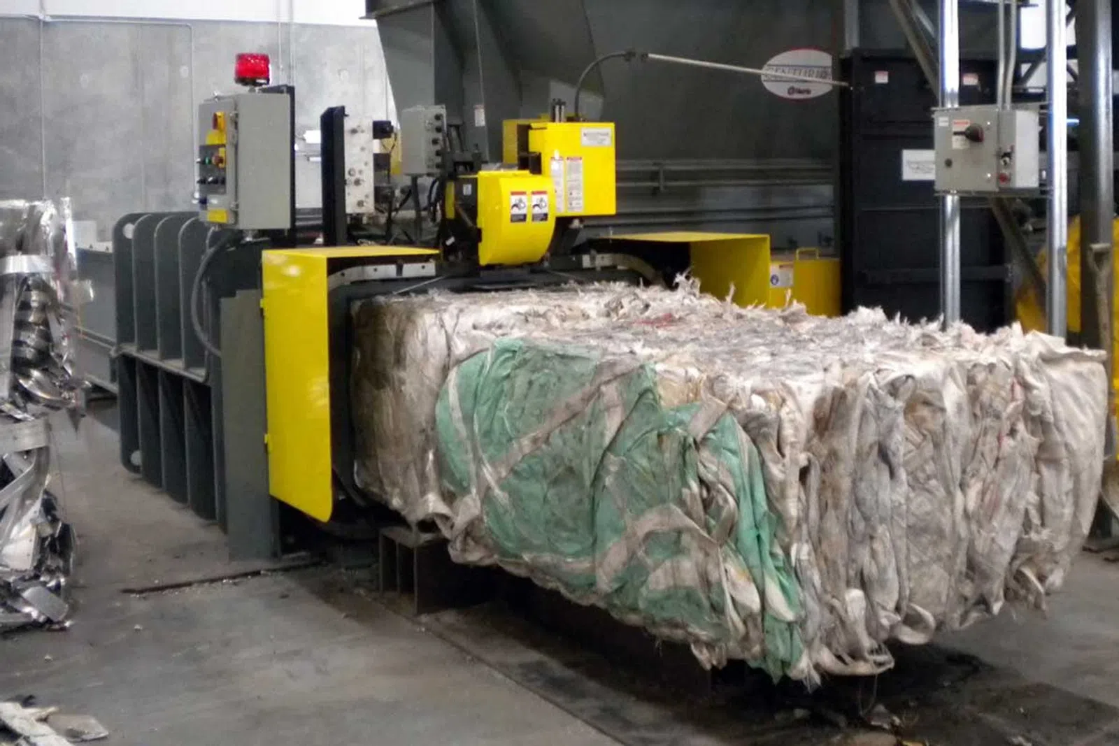 Industrial machine compressing large bales of fabric or plastic waste in a recycling facility.