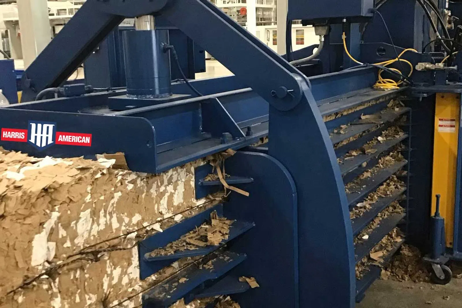 Large industrial blue machine compressing shredded cardboard into compact bales in a warehouse.