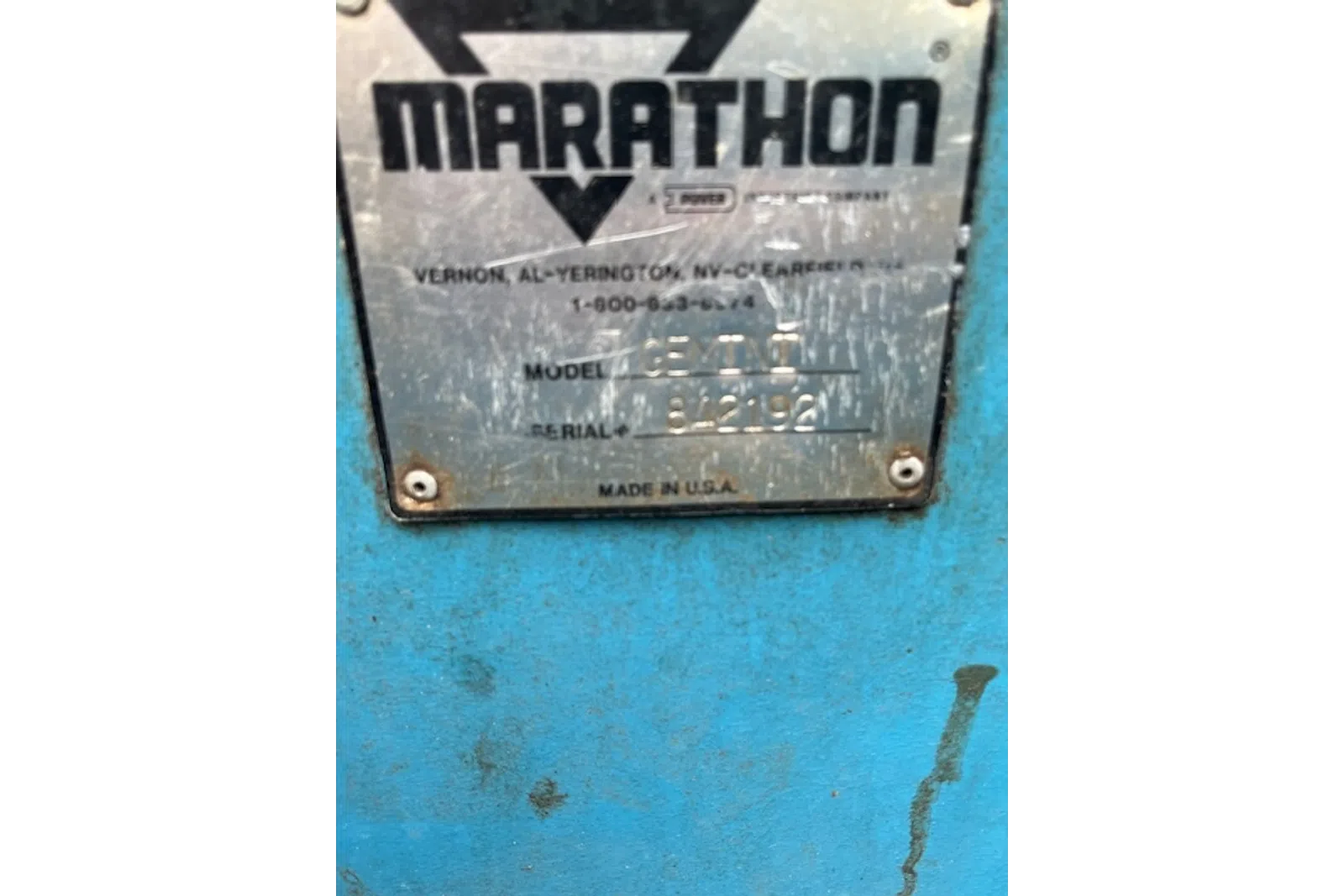 Close-up of scratched Marathon equipment label showing model and serial number on blue metal surface.