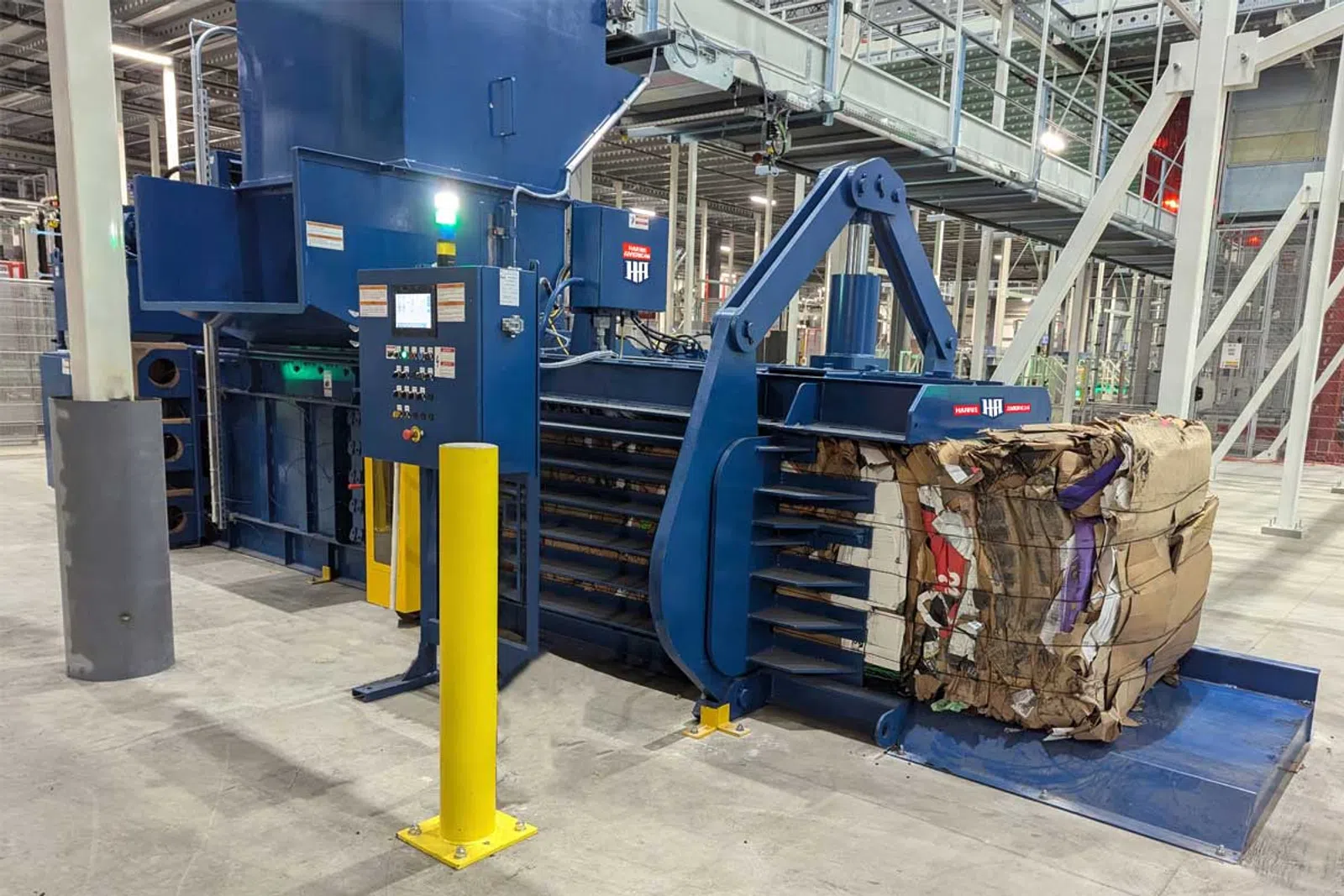 Large industrial baler compressing cardboard and paper waste into a compact block inside a recycling facility