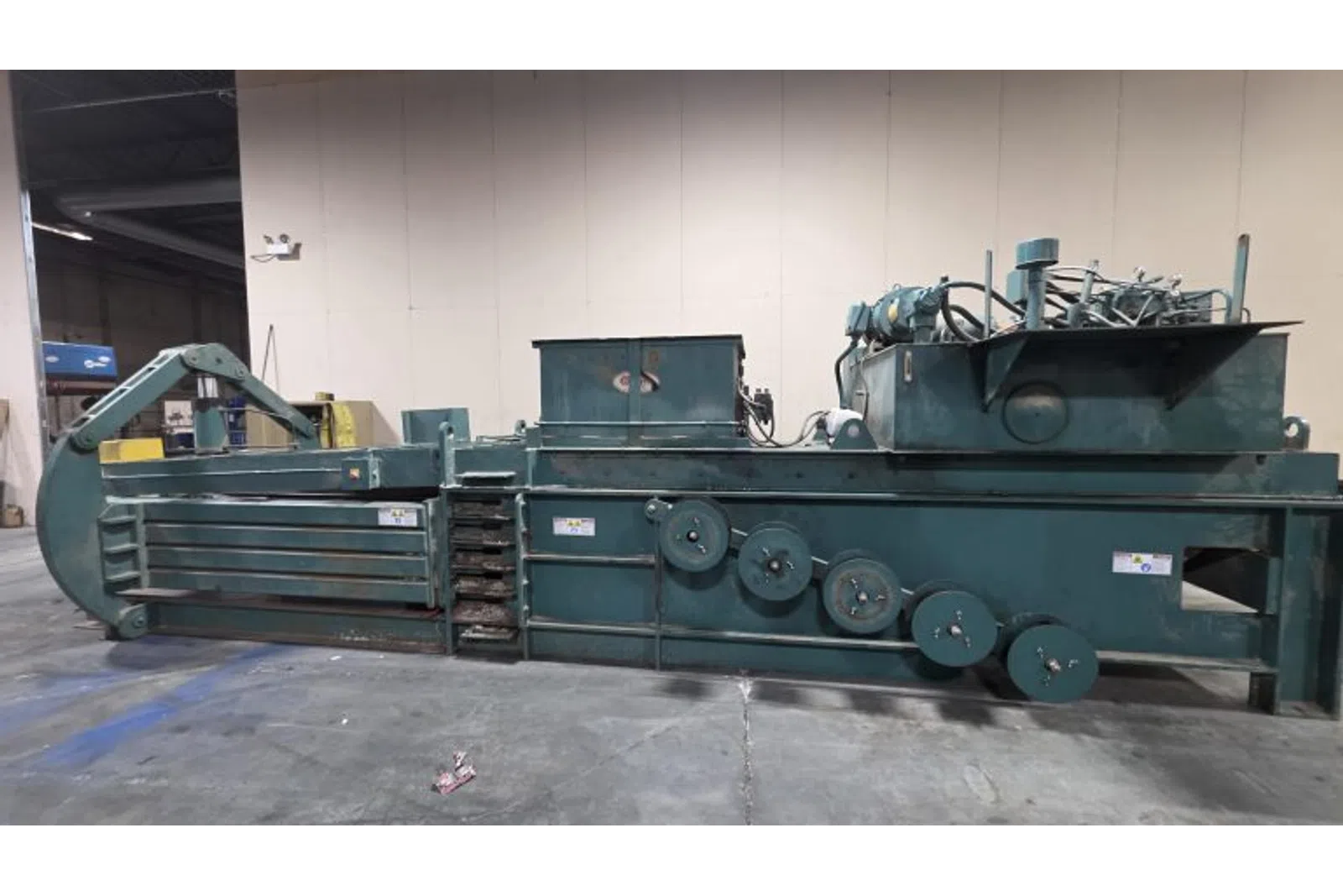 Large industrial green metal baler machine inside a warehouse on concrete floor, used for compacting materials.