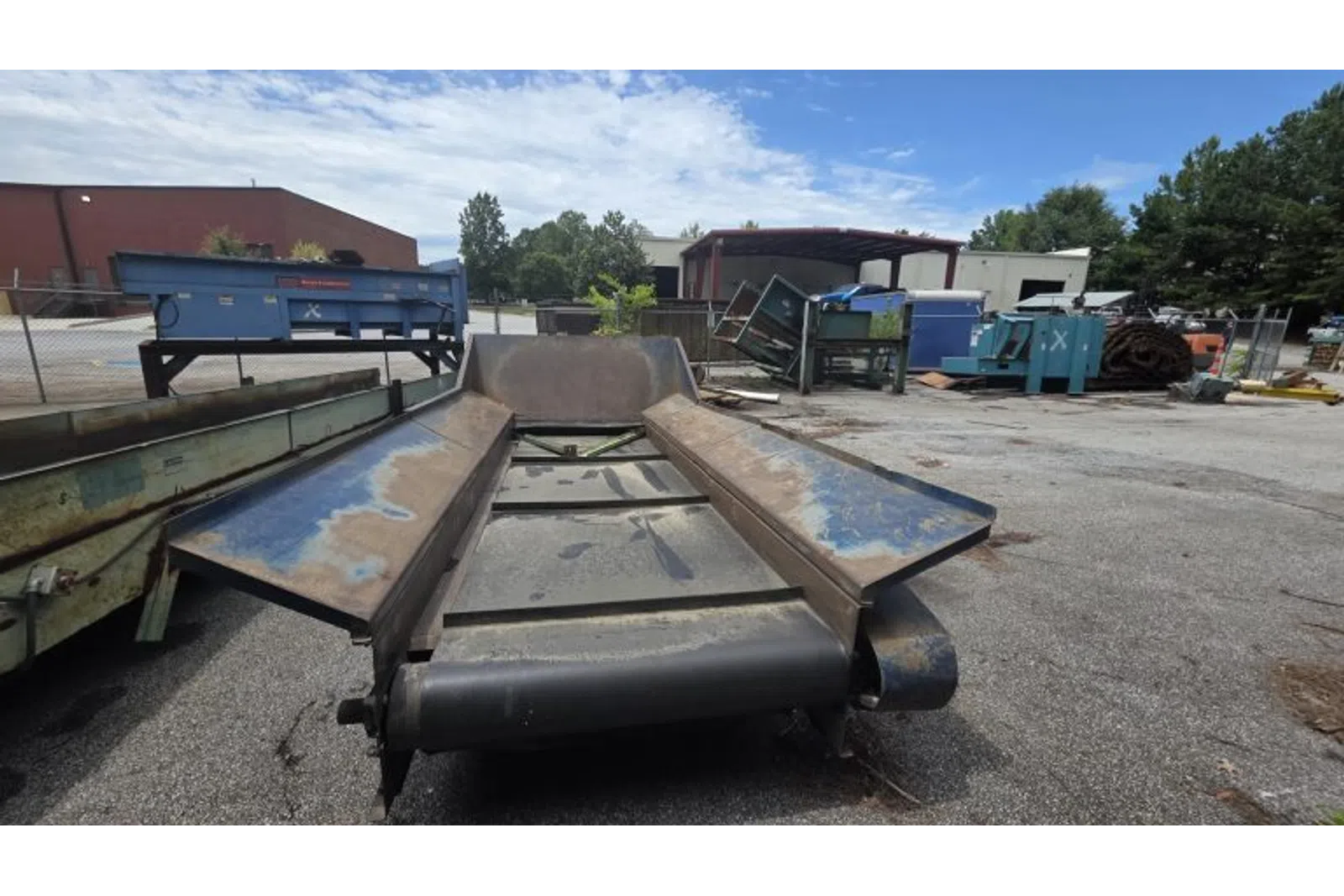 Industrial conveyor belt system outdoors with weathered metal components under a partly cloudy sky.