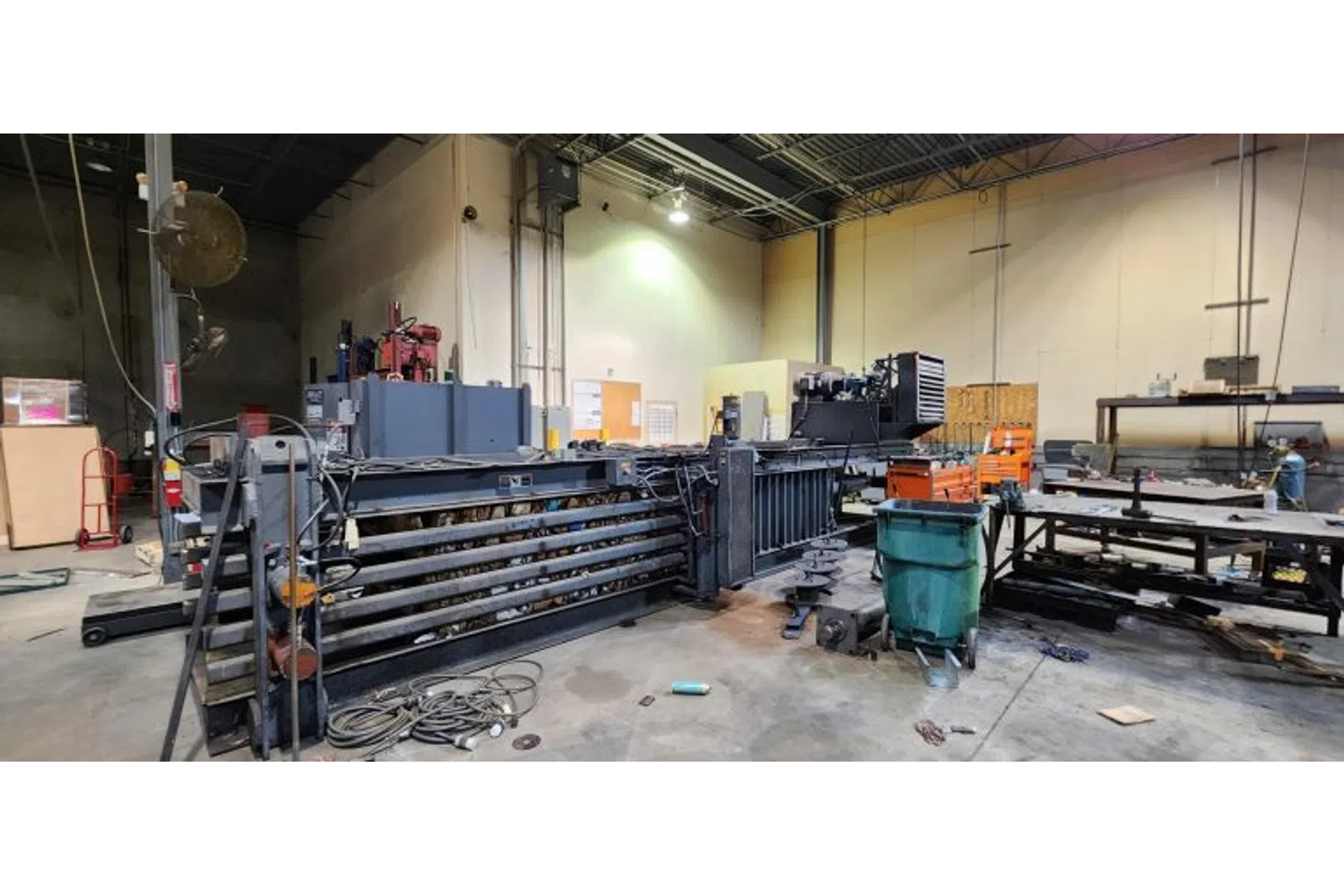 Industrial workshop with large machinery, metal tables, tools, and equipment under bright overhead lights.