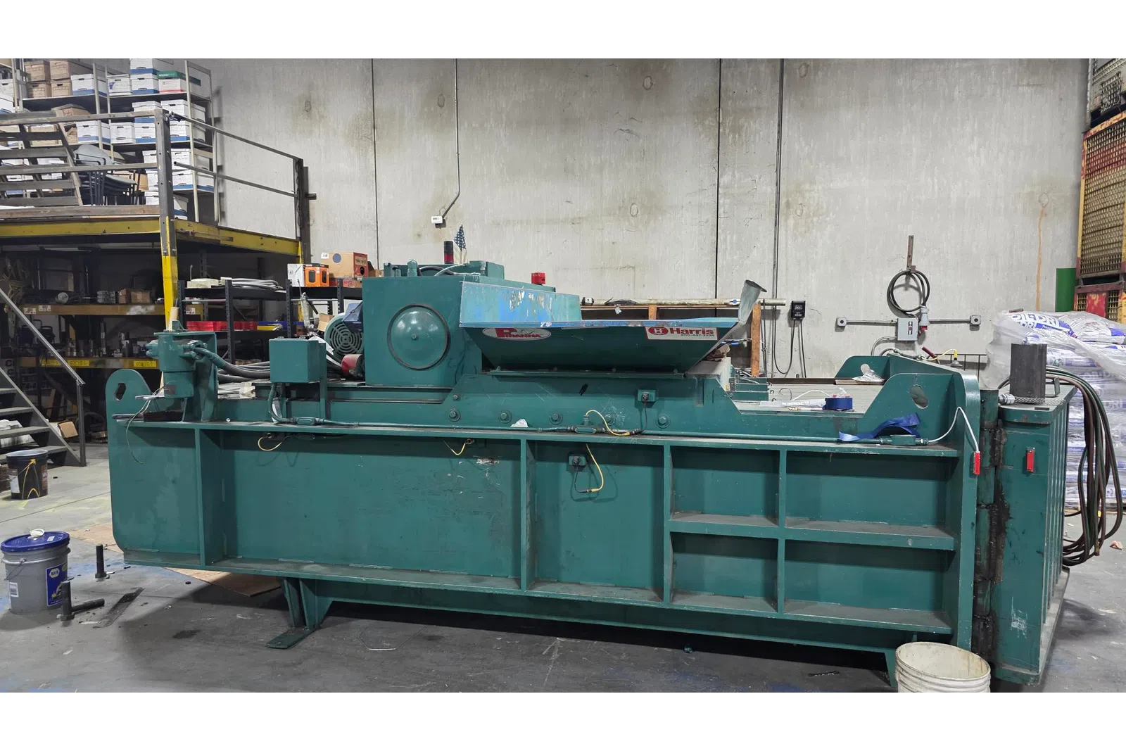 Industrial green machine with rotating mechanism in a warehouse with shelves and equipment.