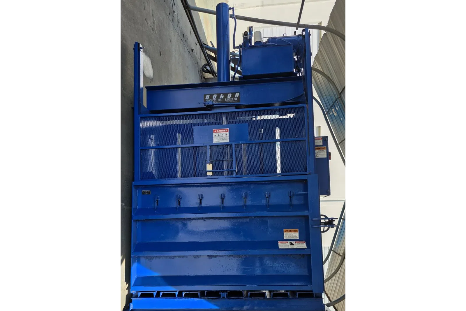 Large blue industrial Selco product machine with safety grills and warning labels in a sheltered outdoor area.