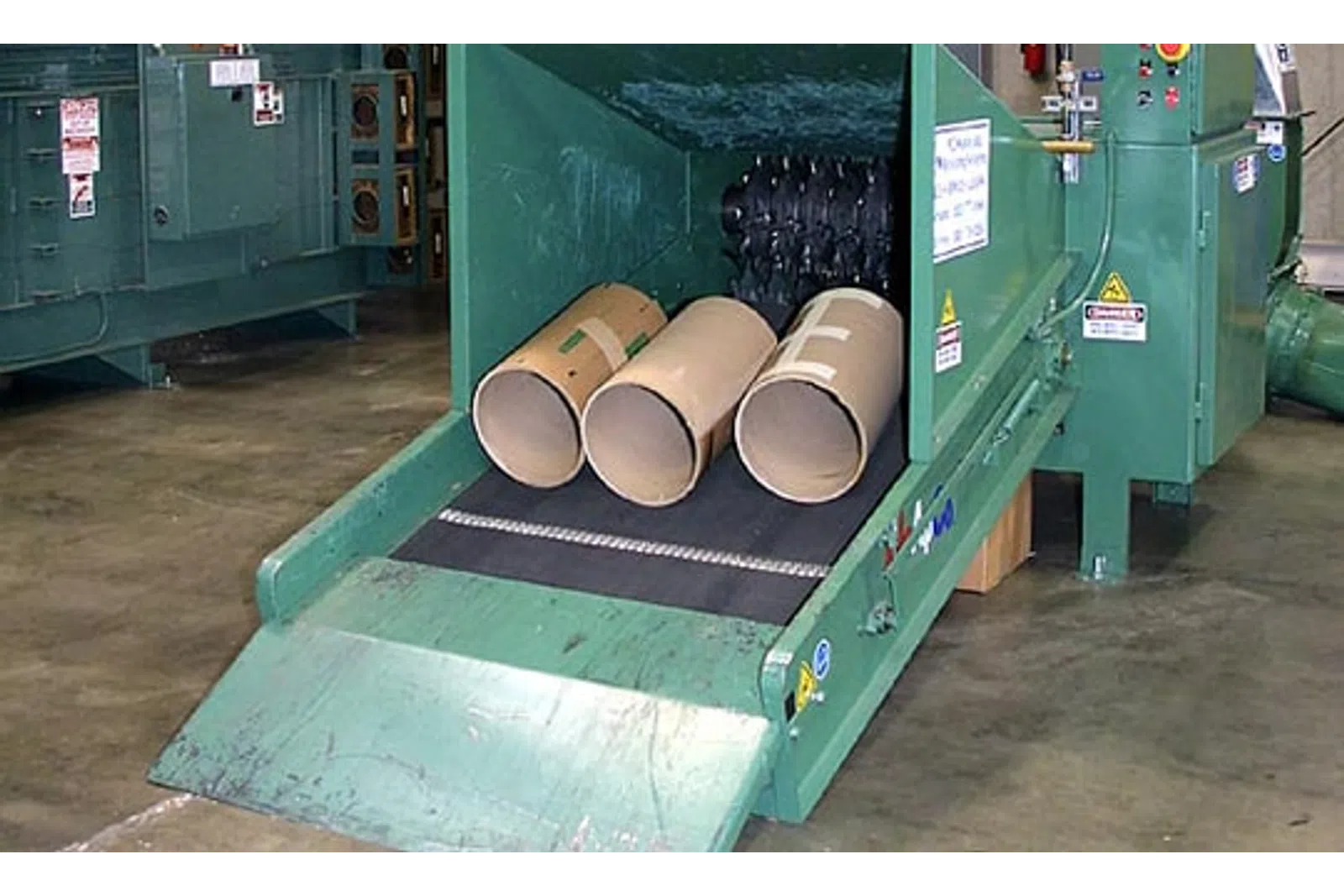 Industrial paper tube shredding machine processing large cardboard tubes on a factory floor conveyor belt.