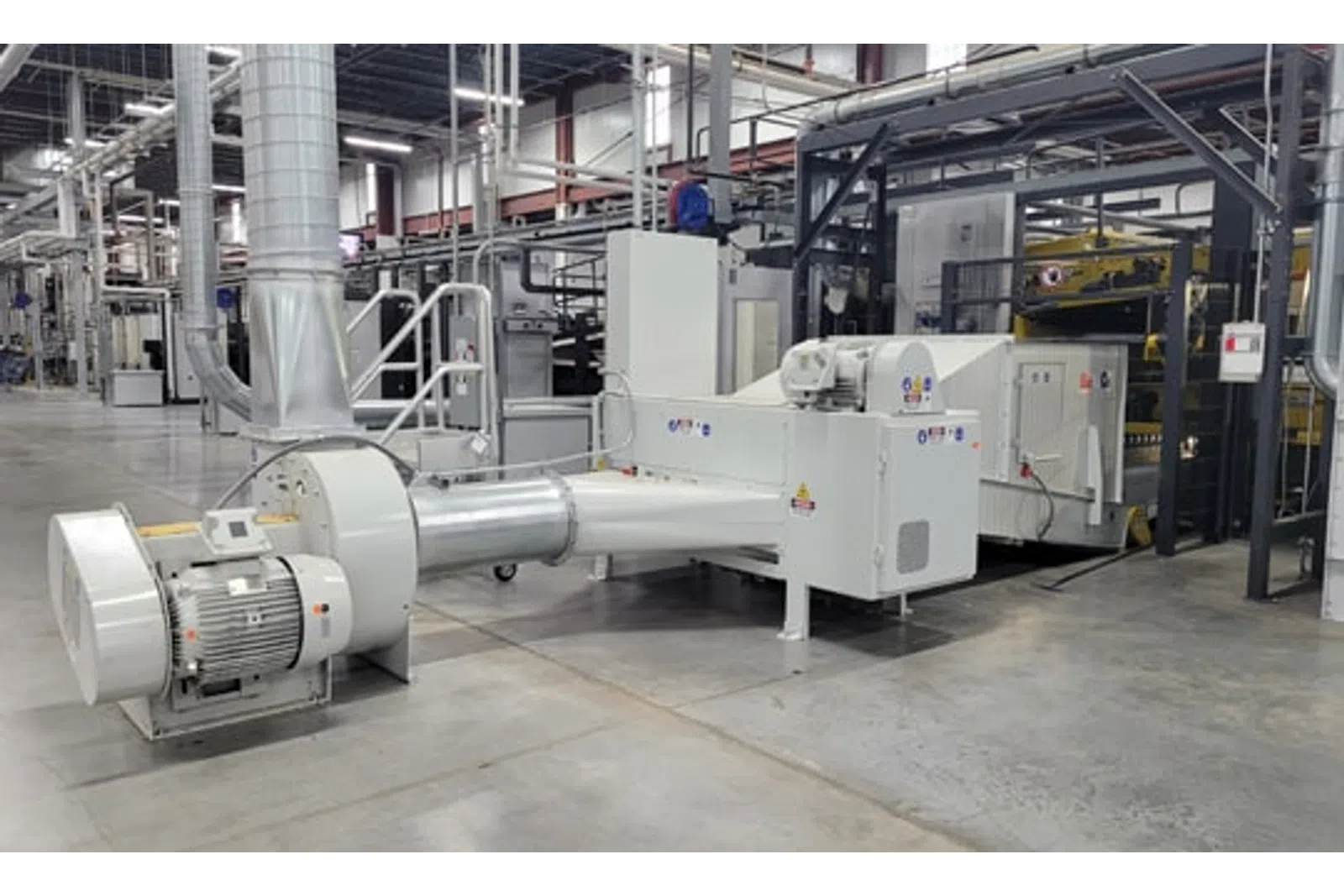 Large industrial machine with motor and ducting in a clean modern factory setting.