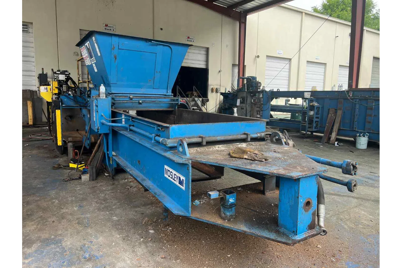 Blue Mosley industrial metal baler machine in a warehouse with open hopper and conveyor.