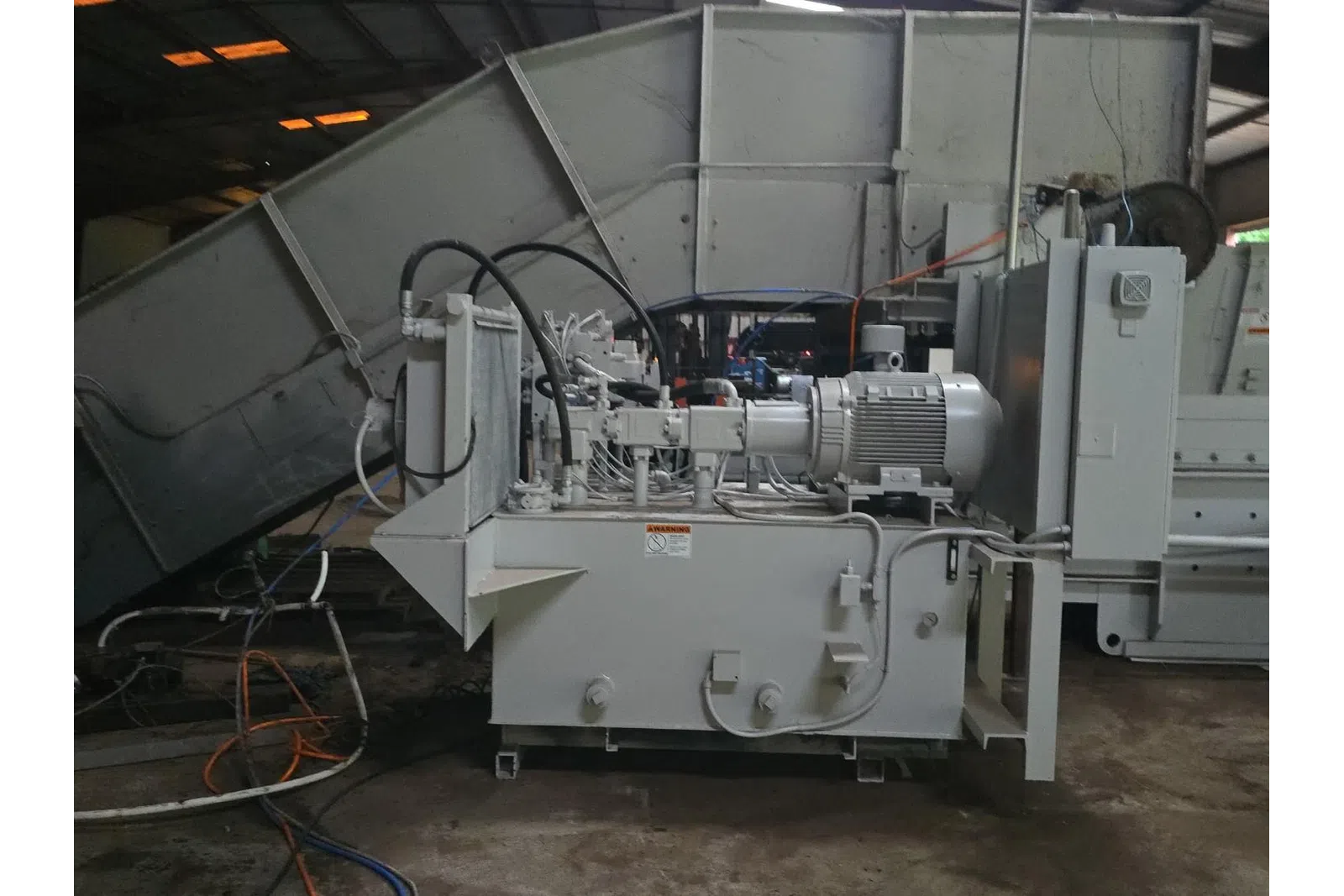 Industrial hydraulic power unit with motor, hoses, and control components in factory setting.