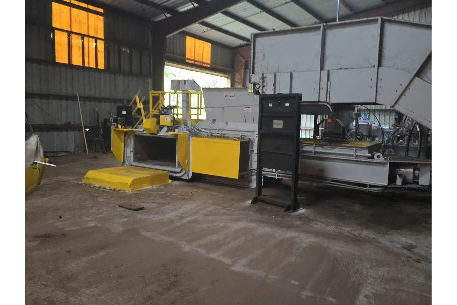 Industrial machinery with yellow panels inside a large factory with high ceilings and orange windows.