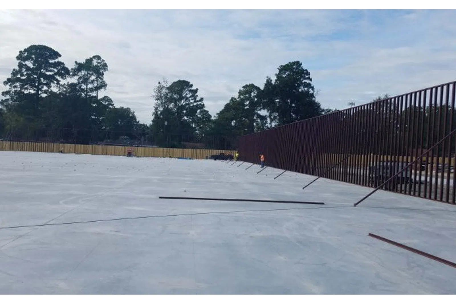 Large concrete slab with a tall metal fence along one side and trees in the background under a cloudy sky