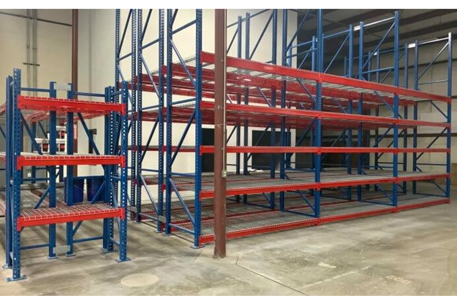 Empty industrial blue and red metal storage racks on a concrete floor inside a warehouse.