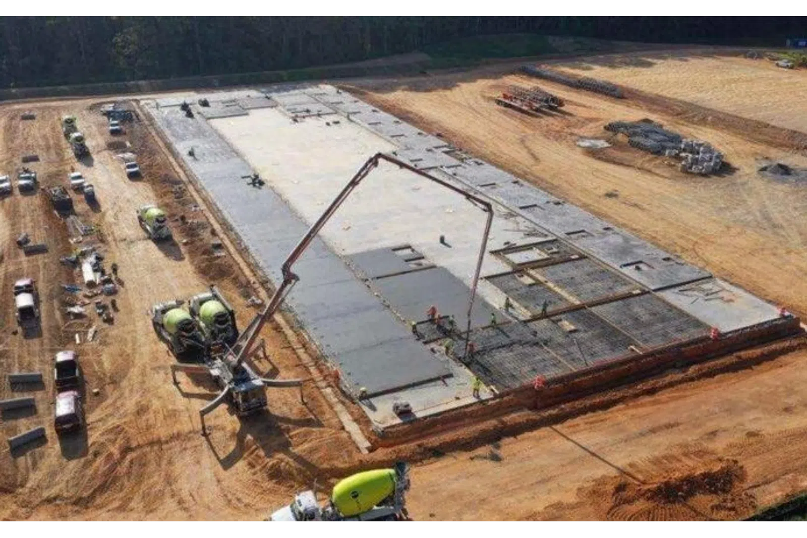 Aerial view of a large concrete slab foundation being poured at a construction site with multiple cement mixers.