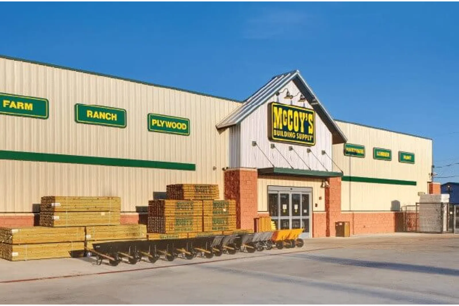 Exterior view of McCoy's Building Supply store with stacked lumber and wheelbarrows outside under clear sky