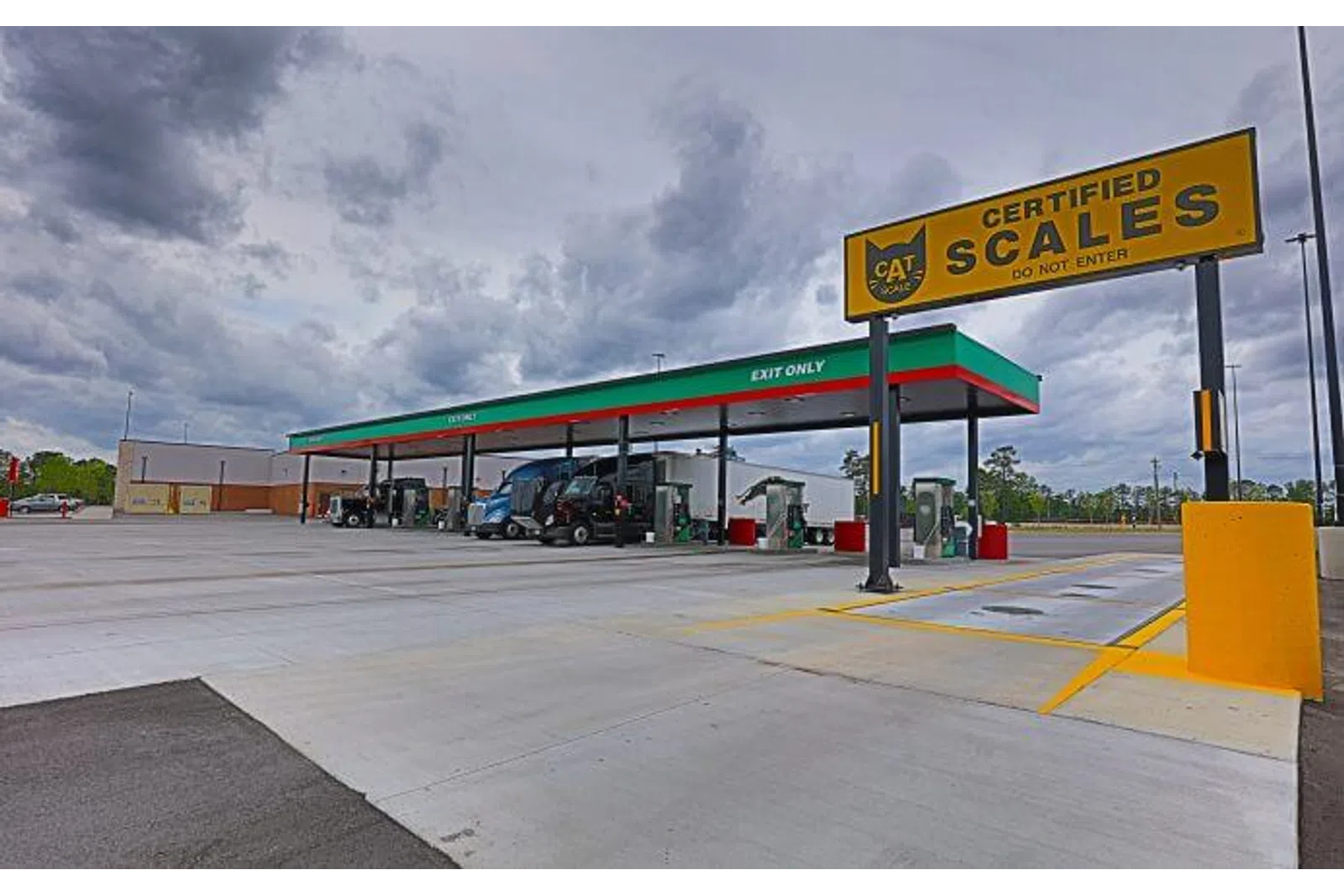 Truck stop with multiple fuel pumps under canopy and a large certified scales sign on a cloudy day