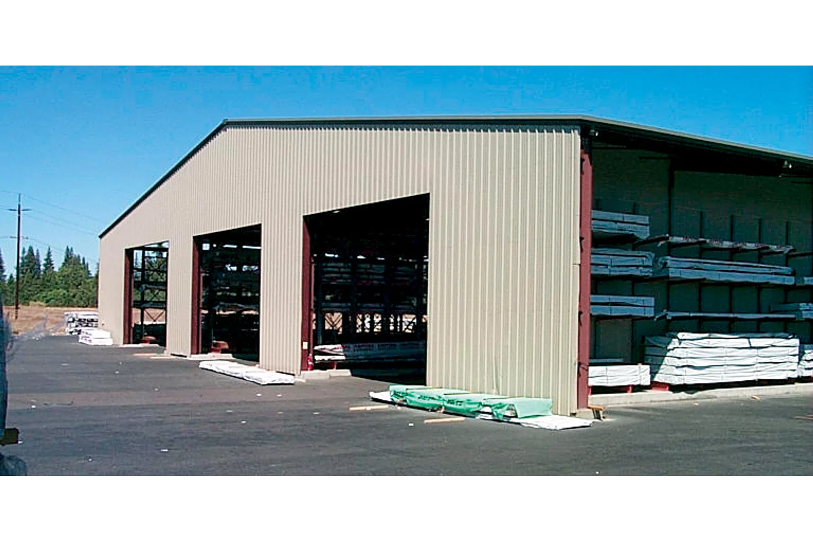 Large outdoor storage warehouse with metal siding storing lumber and construction materials on racks.