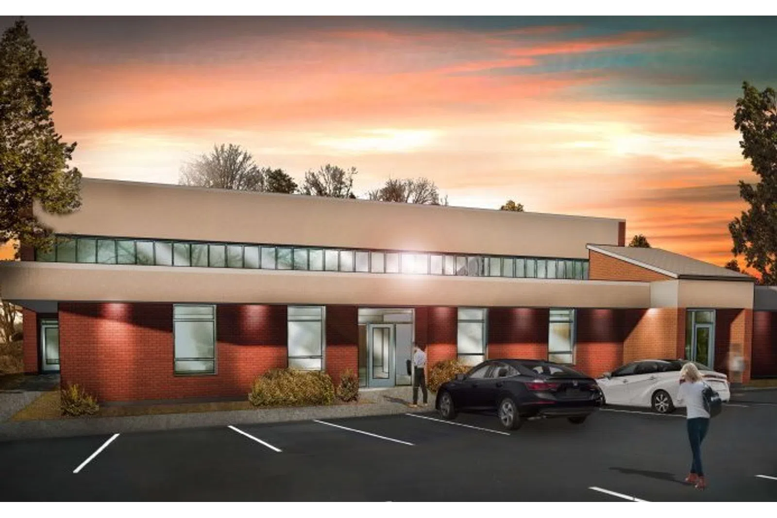 Modern single-story brick office building with cars parked and people walking at sunset with colorful sky.