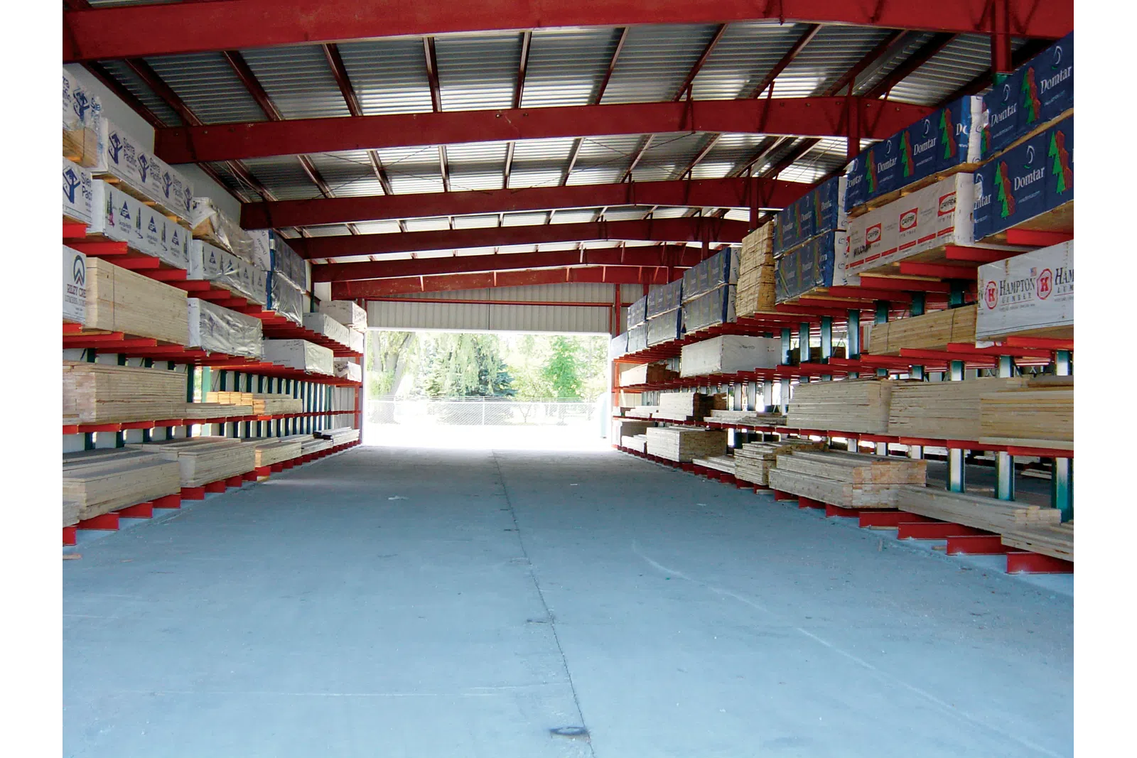 Warehouse with organized shelves storing lumber and building materials under a red steel roof structure.