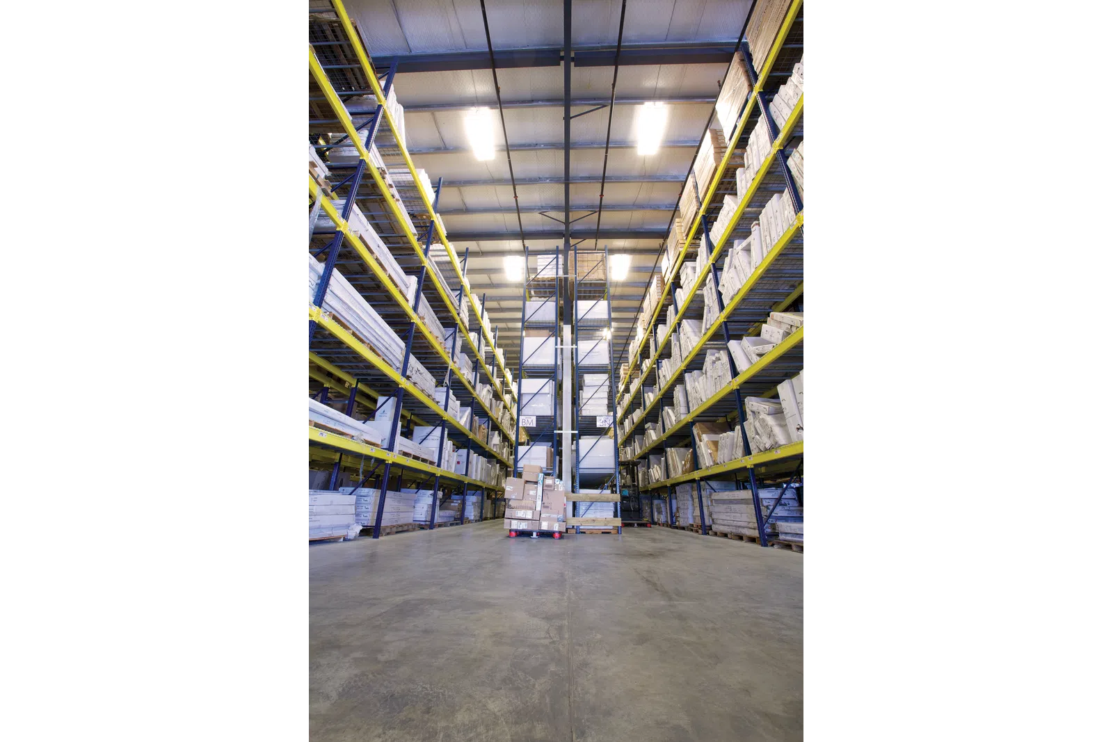 Interior of a large warehouse with tall shelves stocked with boxes and packages on a concrete floor.