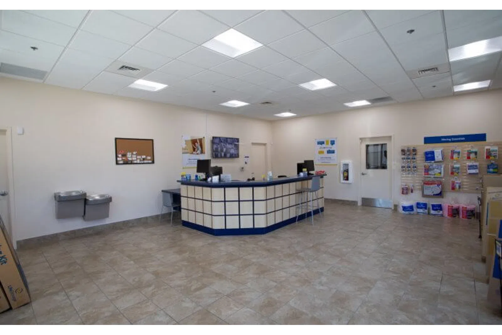 Clean postal service counter area with tiled floor, information display, and water fountains in a bright room.