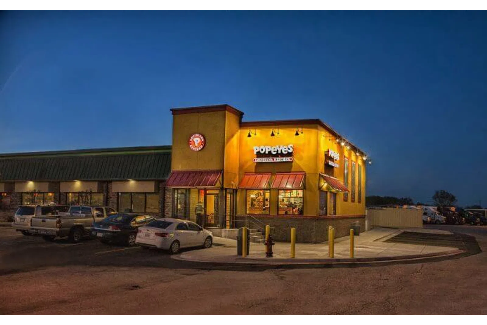 Popeyes Louisiana Kitchen restaurant lit up at night with cars parked outside in the parking lot.