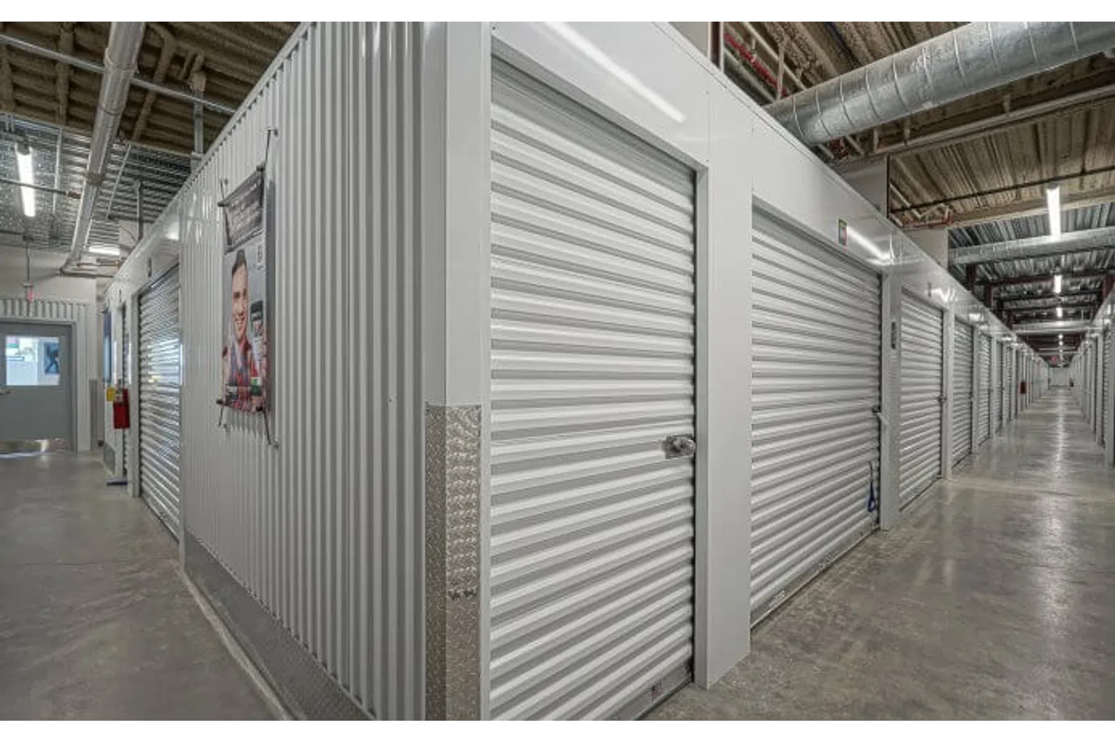 Interior view of a self storage facility with rows of closed metal roll-up doors and a concrete floor.