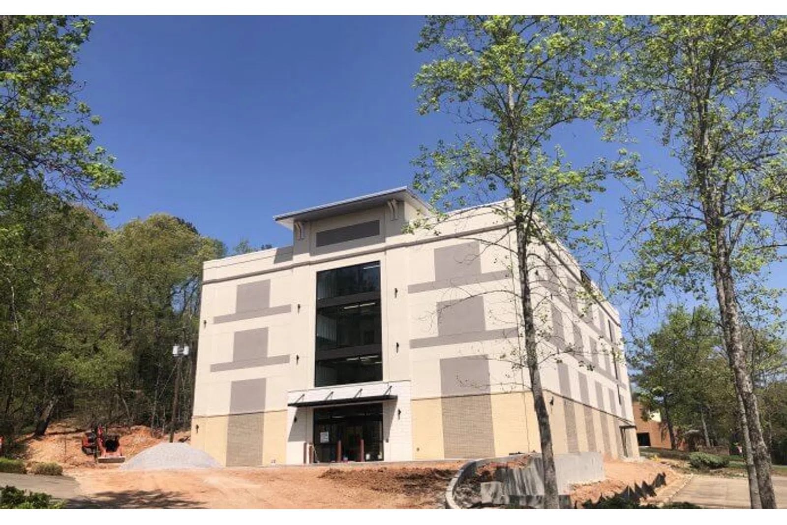 Newly constructed beige commercial building surrounded by trees under a clear blue sky.