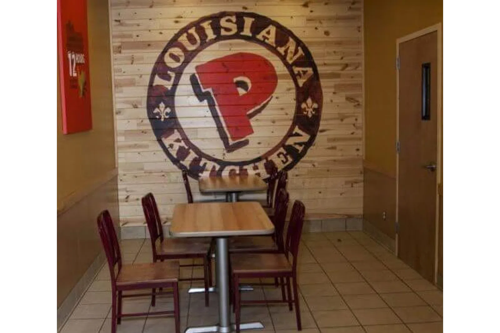 Interior of a Popeyes Louisiana Kitchen with wooden tables, chairs, and large logo mural on wood wall.