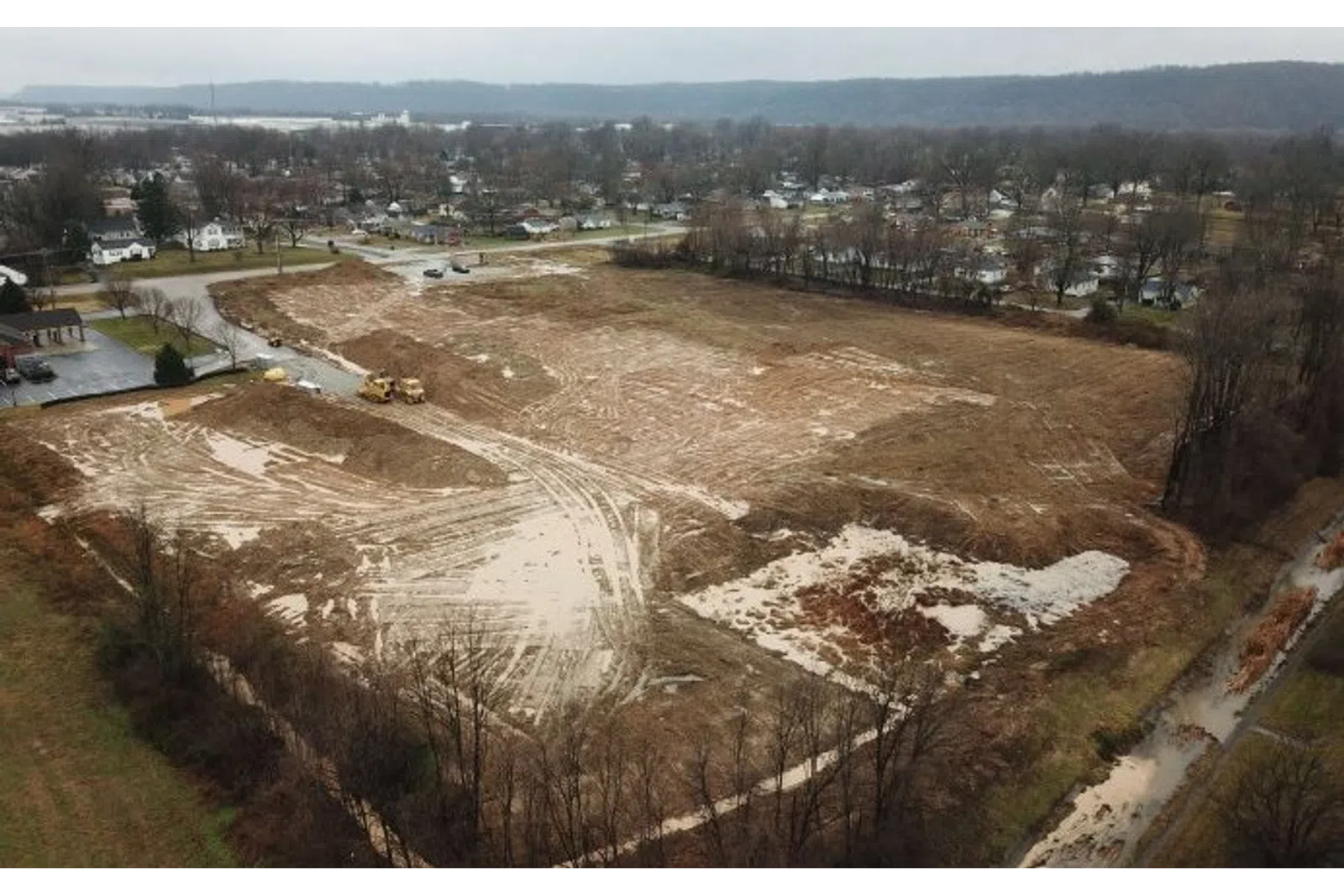 Cleared and leveled construction site with earthmoving equipment near residential area under cloudy sky