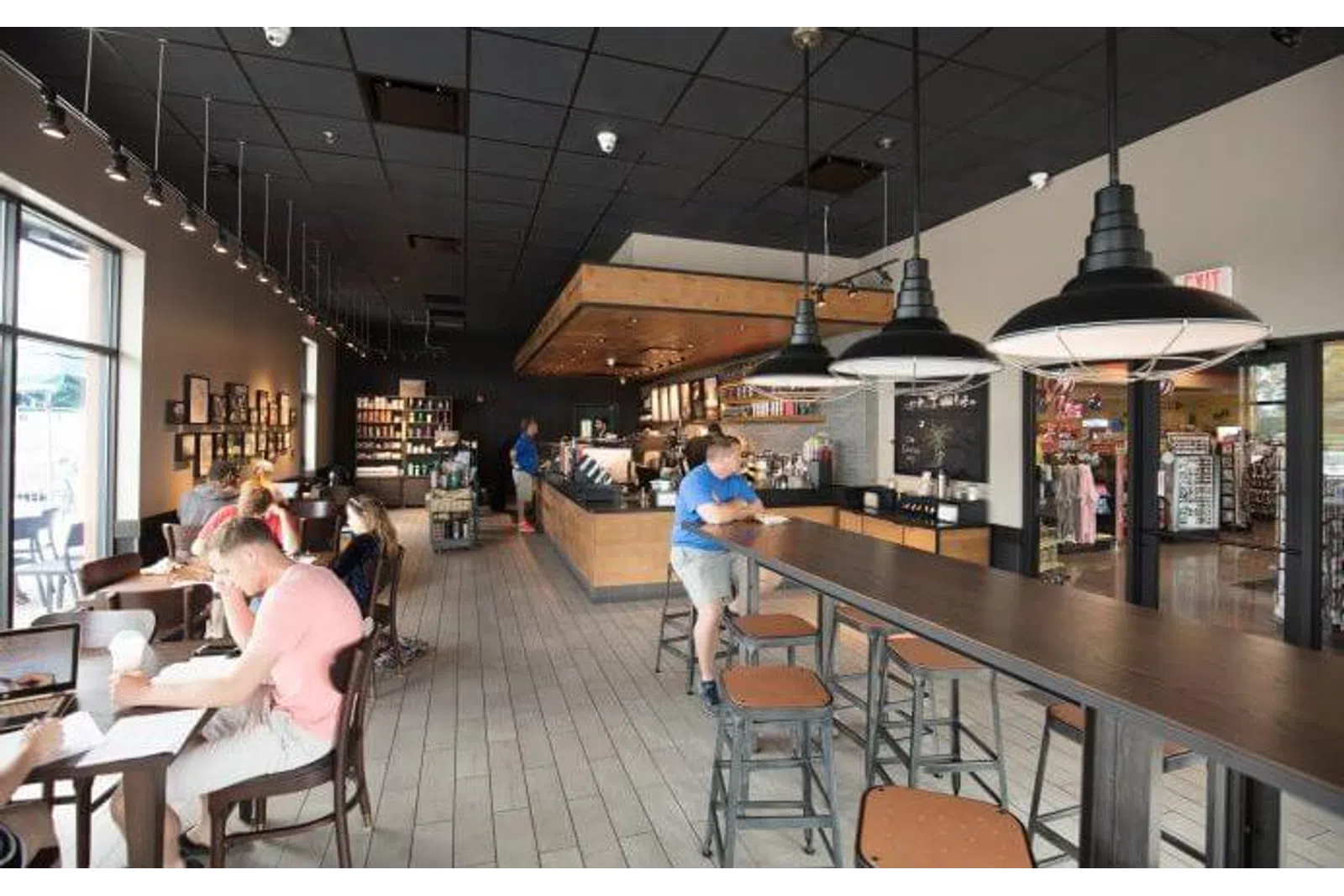 Modern coffee shop interior with wooden tables, pendant lights, customers working and ordering coffee.