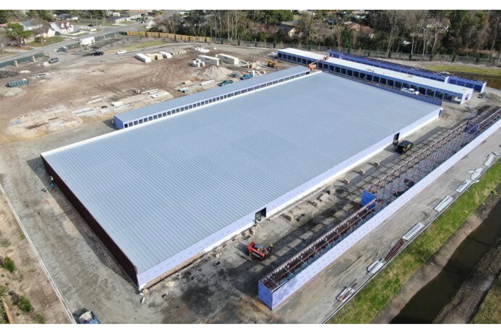 Aerial view of a large metal-roofed warehouse under construction with surrounding construction equipment and materials.