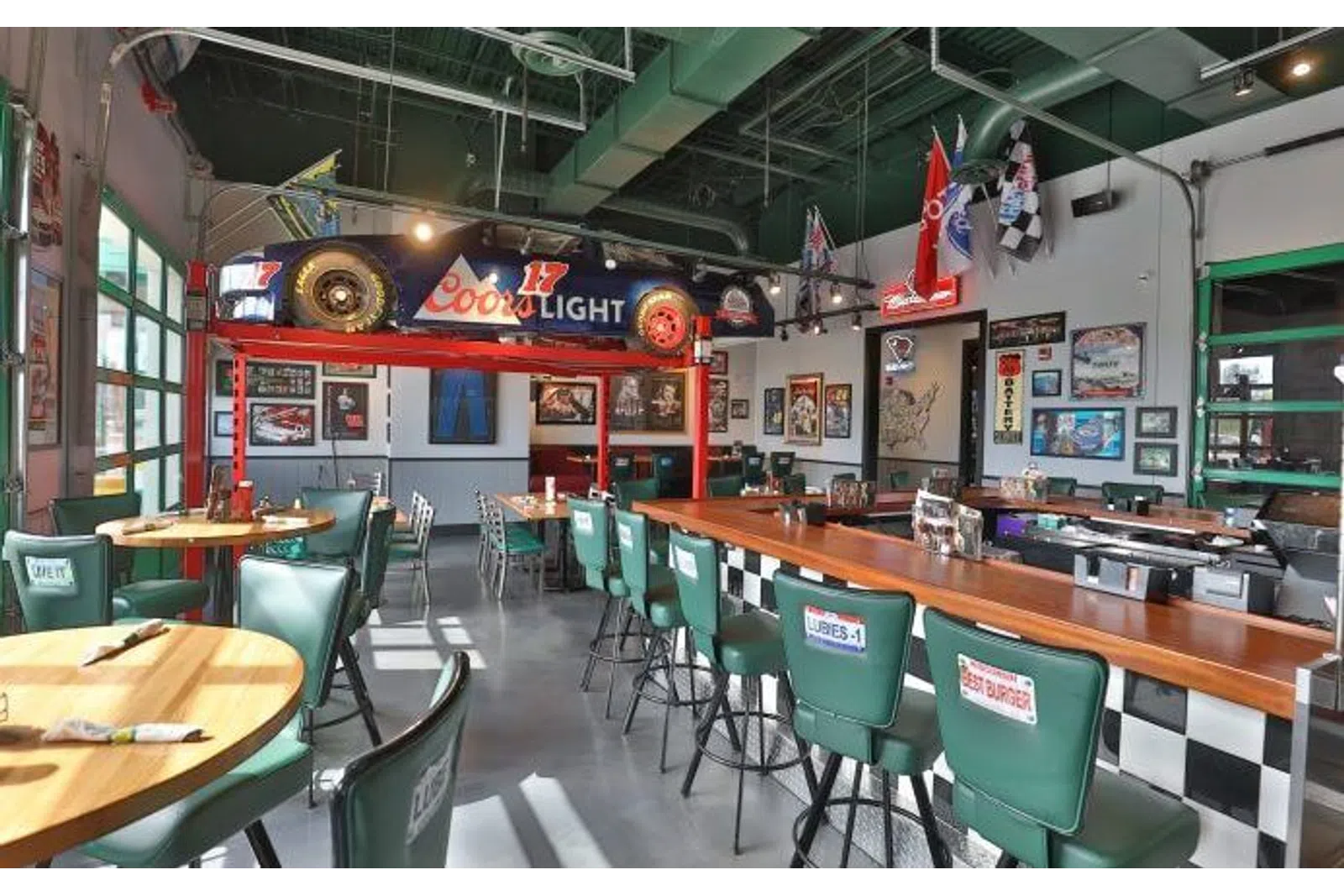 Retro diner interior with green chairs, wooden tables, racing memorabilia, and a Coors Light race car display.