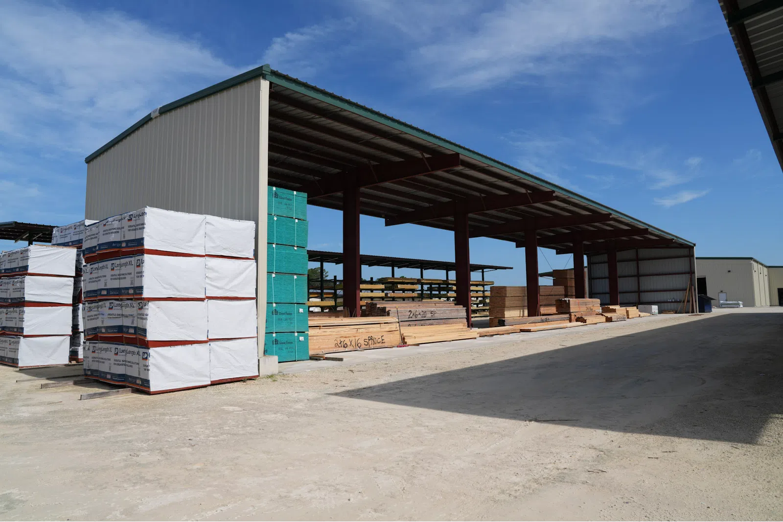 Outdoor lumber yard with stacks of wood and building materials under clear blue sky and metal shelter