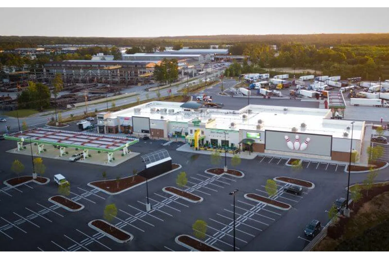 Aerial view of a commercial gas station with attached bowling alley and empty parking lot at sunset.