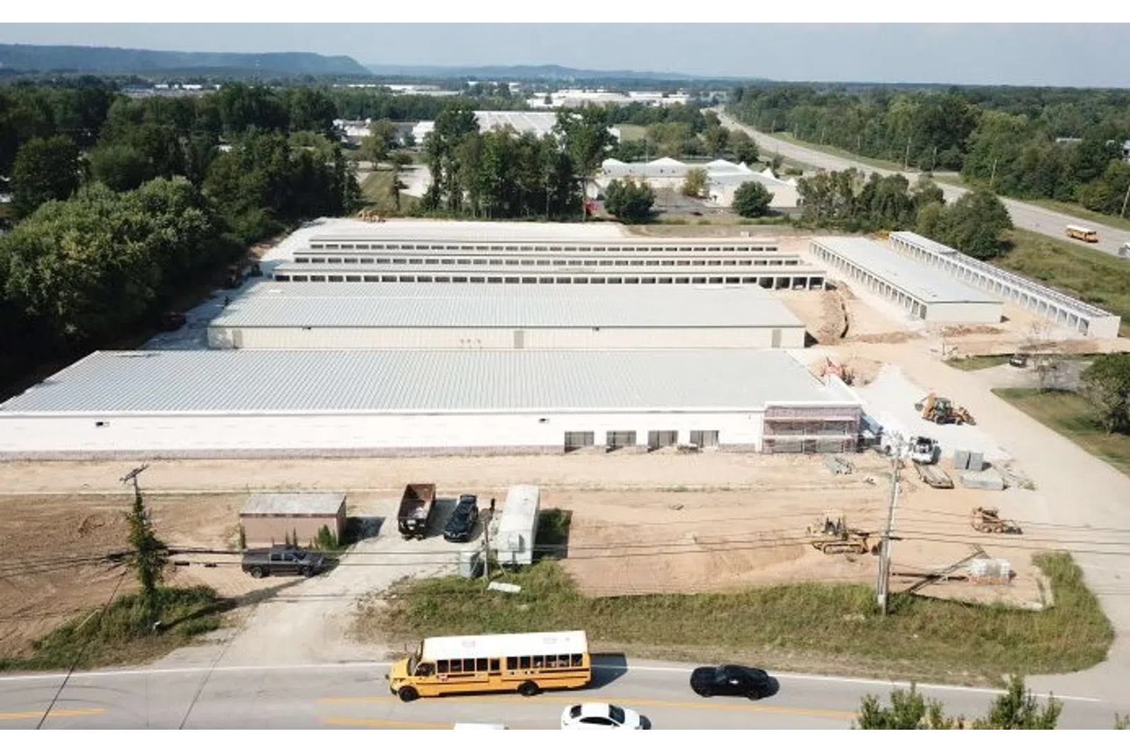 Aerial view of large industrial warehouses under construction with vehicles on adjacent road under clear sky