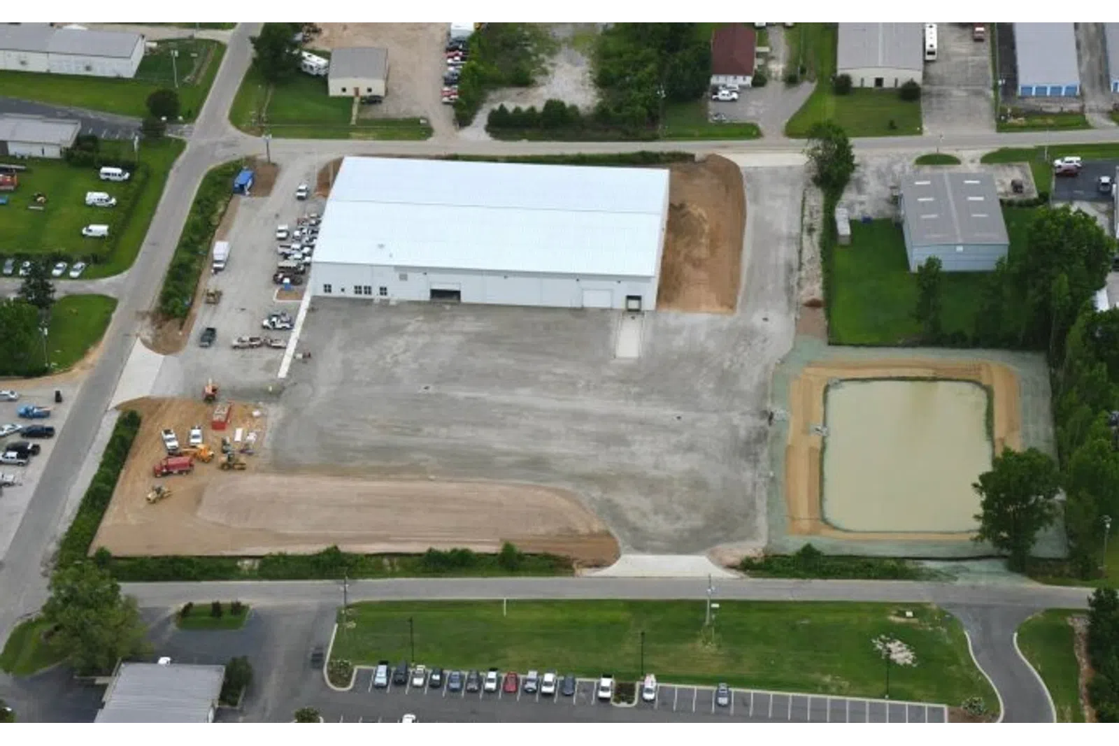 Aerial view of industrial warehouse with adjacent construction site and retention pond in a commercial area.