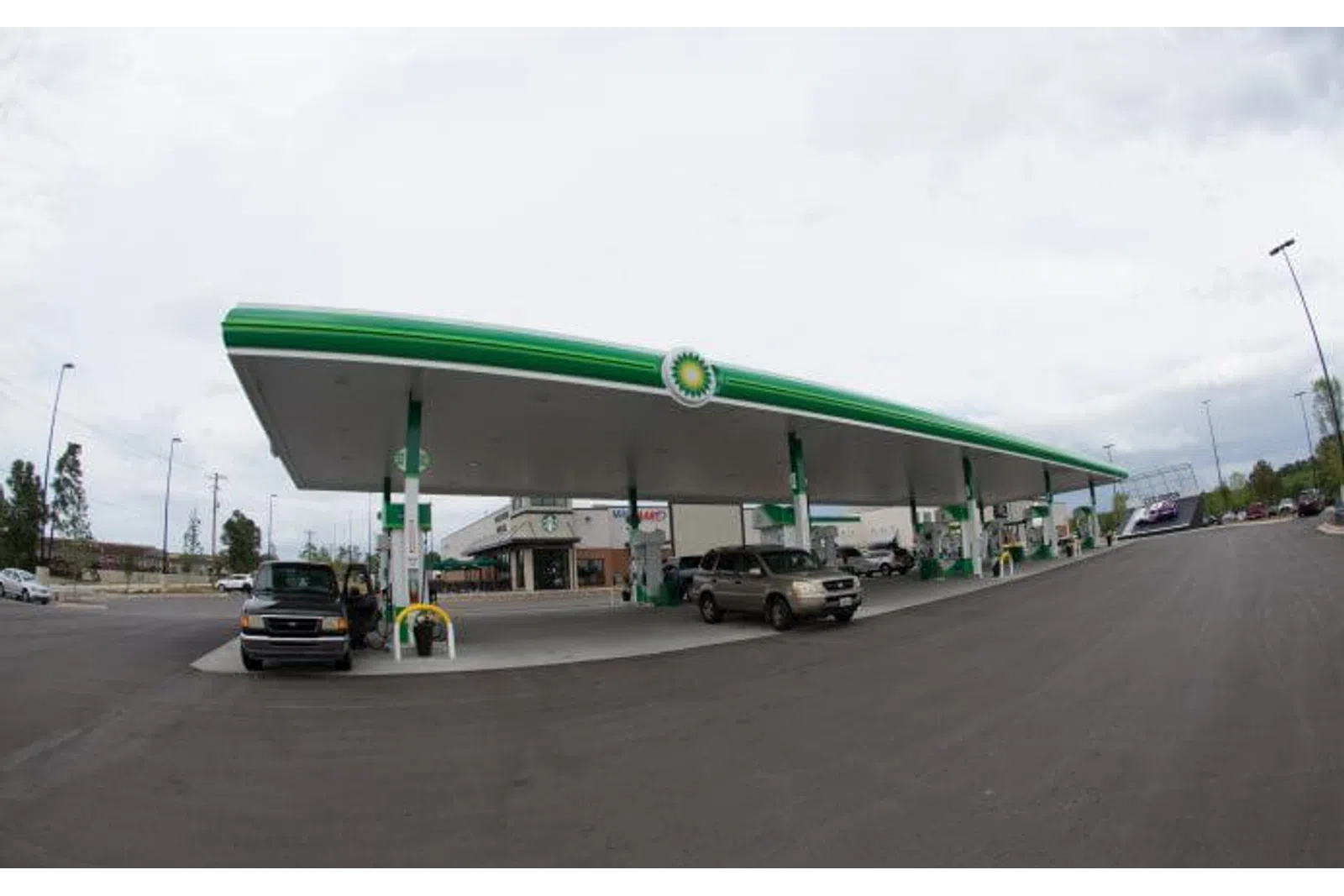 Wide view of a BP gas station with cars refueling under a large green and white canopy on a cloudy day.