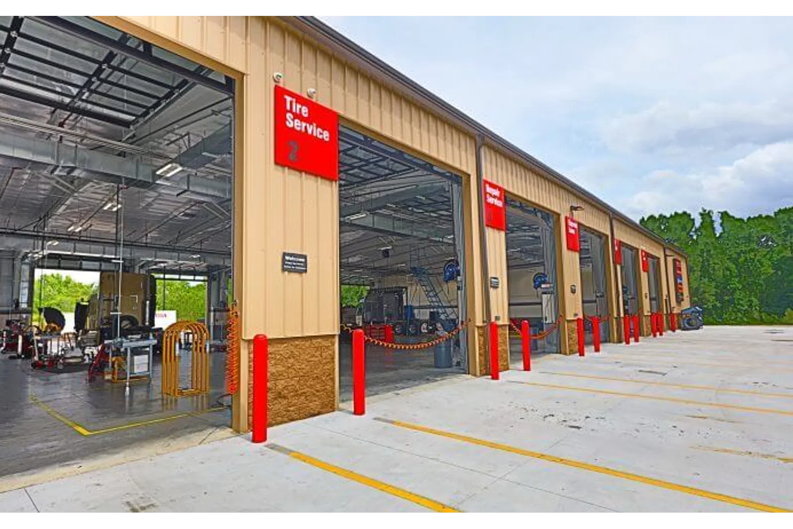 Exterior shot of a multi-bay auto service center with Tire Service and Wheel Service bays open under a clear sky.