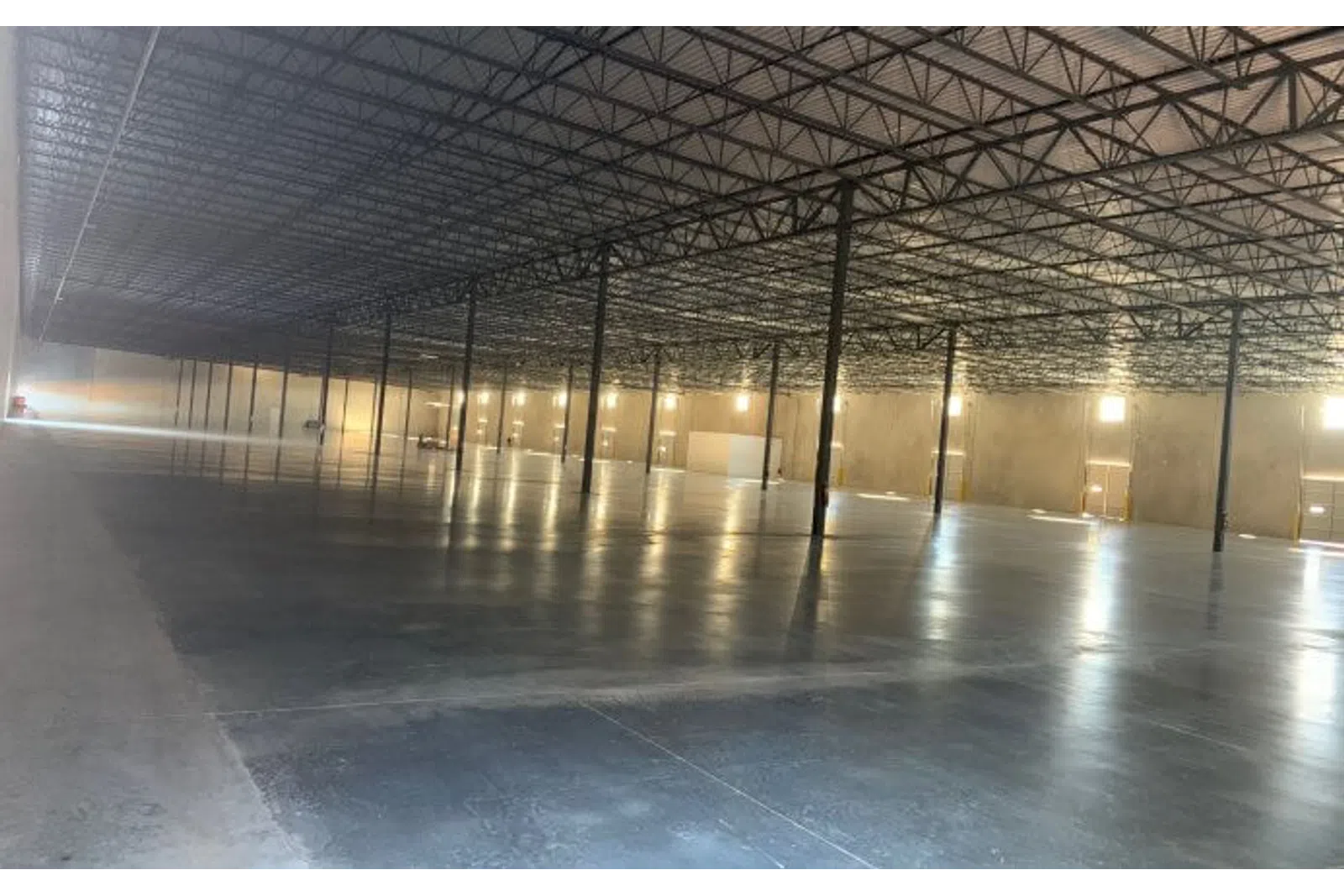 Spacious empty industrial warehouse with polished concrete floor, high ceiling, and metal support beams
