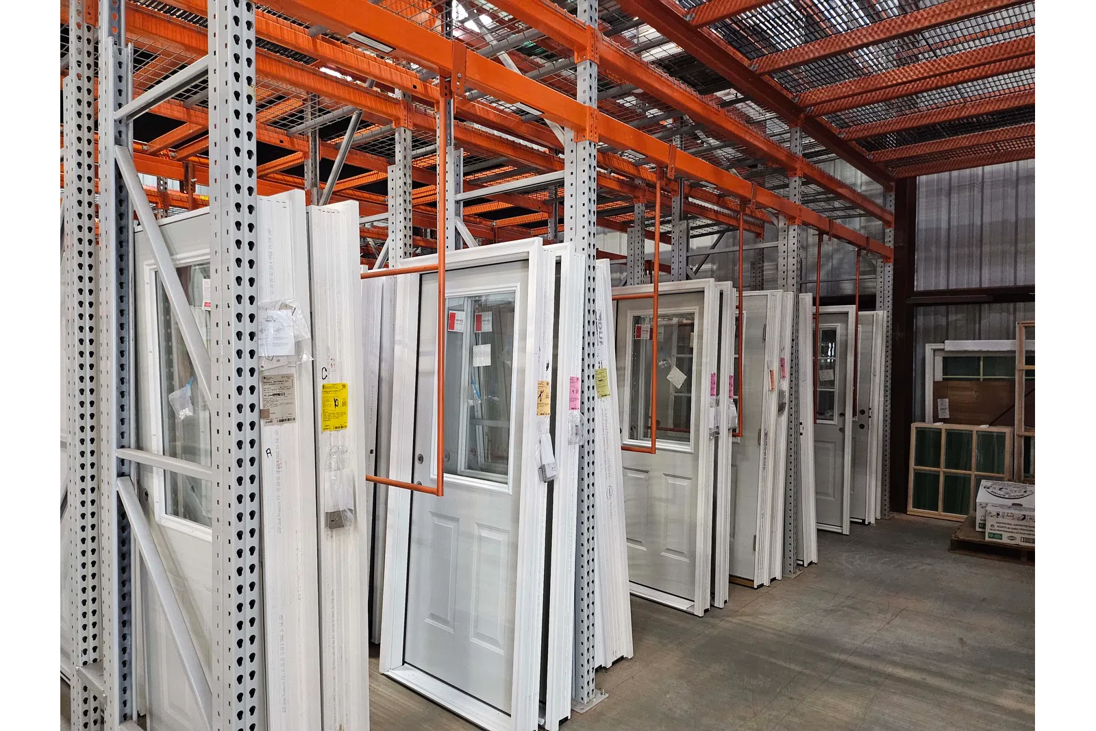 Warehouse shelves storing white exterior doors with windows in an organized industrial setting.