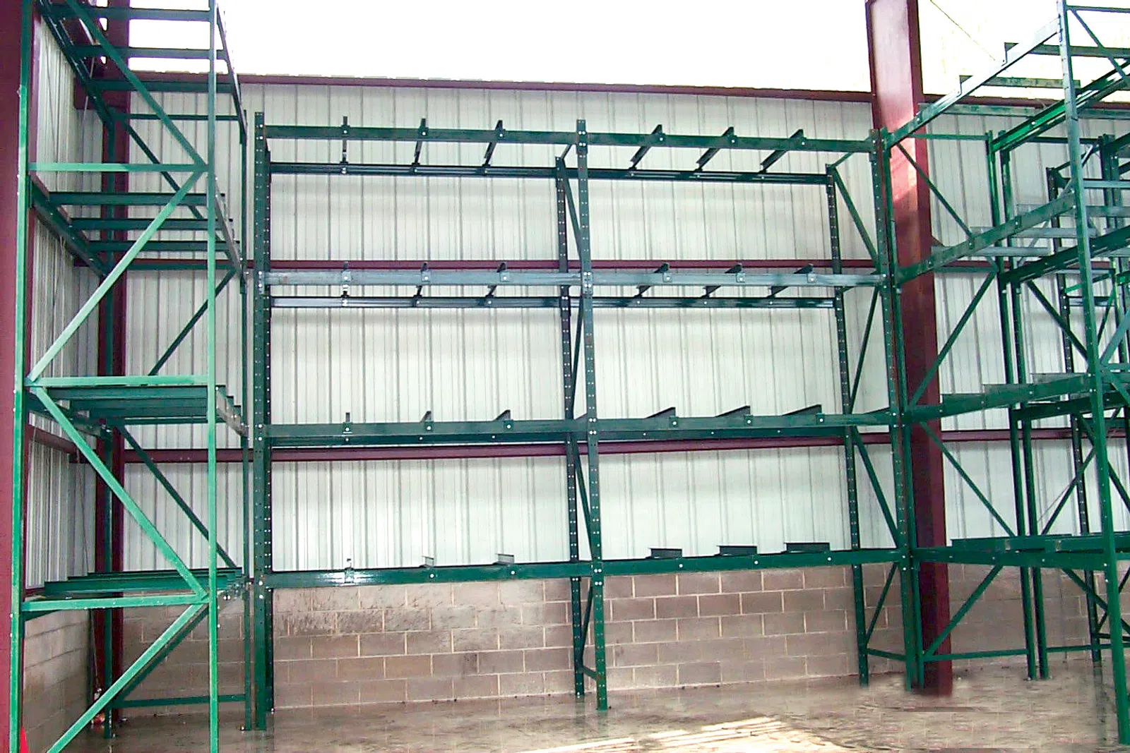 Empty green industrial metal storage racks inside a warehouse with concrete floor and walls.
