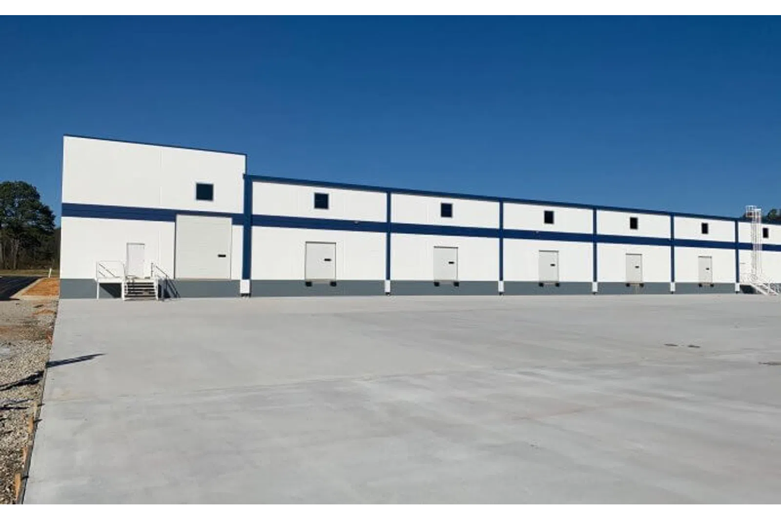 White and blue industrial warehouse with multiple loading dock doors under a clear blue sky