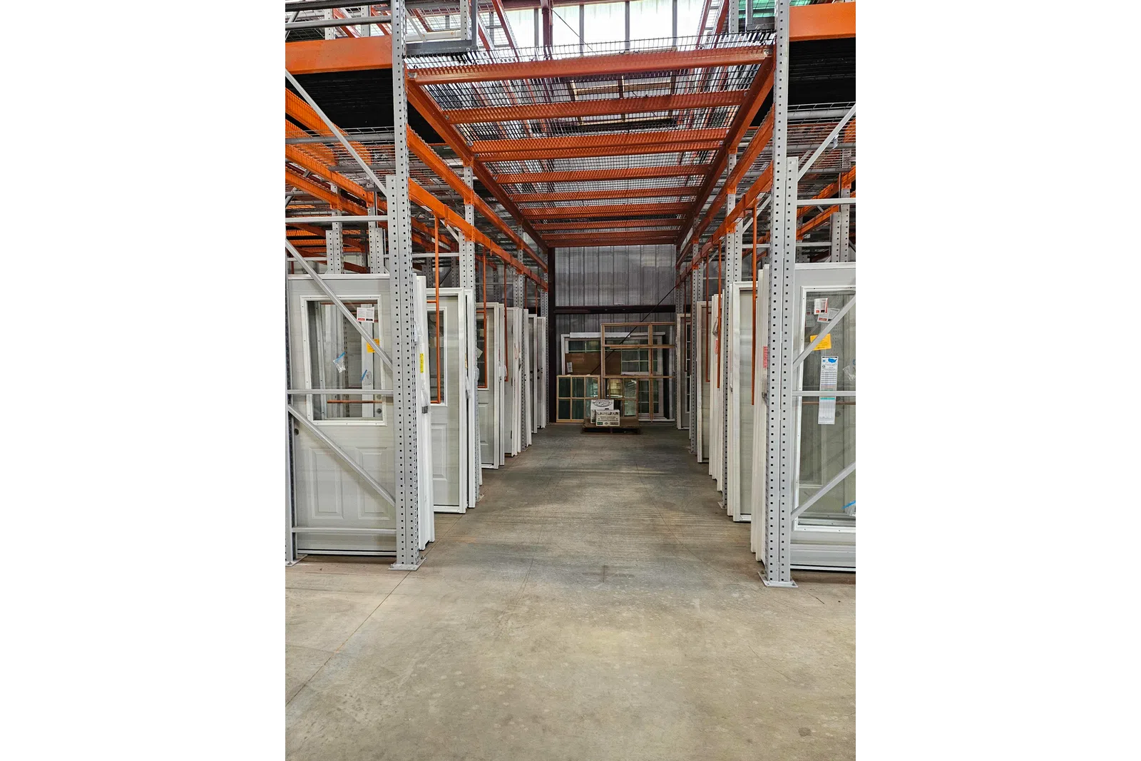 Warehouse aisle with white framed doors and windows stored on metal racks with an orange overhead structure.