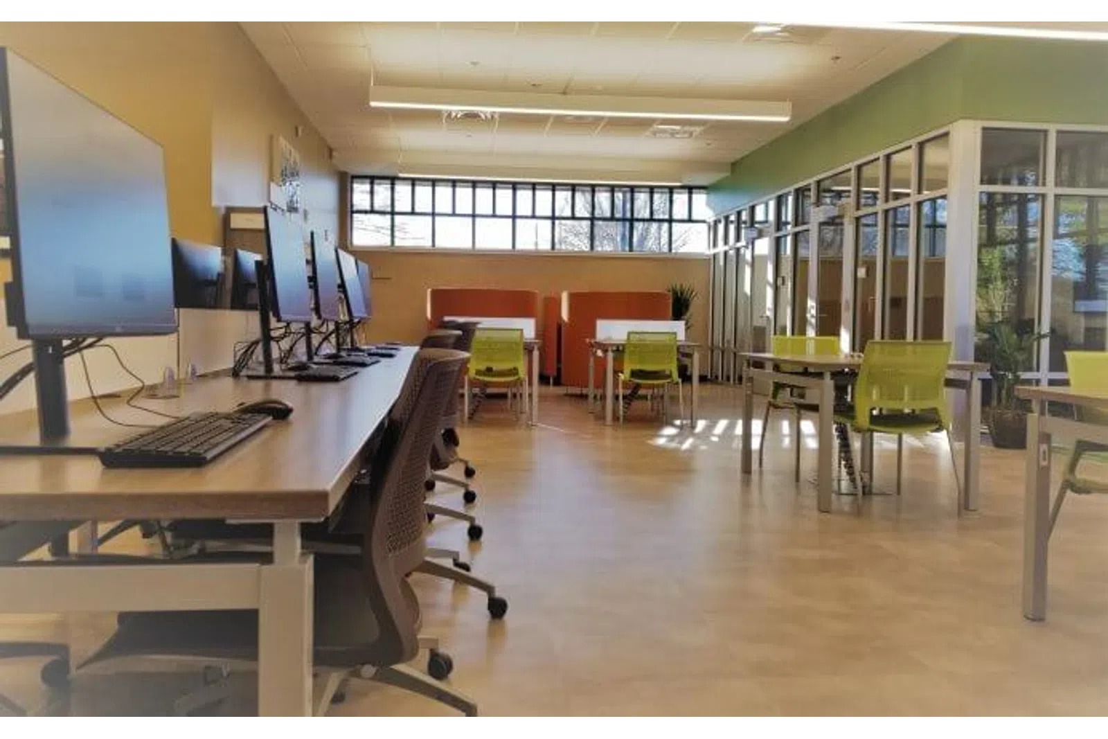 Modern office workspace with multiple computer stations, ergonomic chairs, and natural light through large windows.