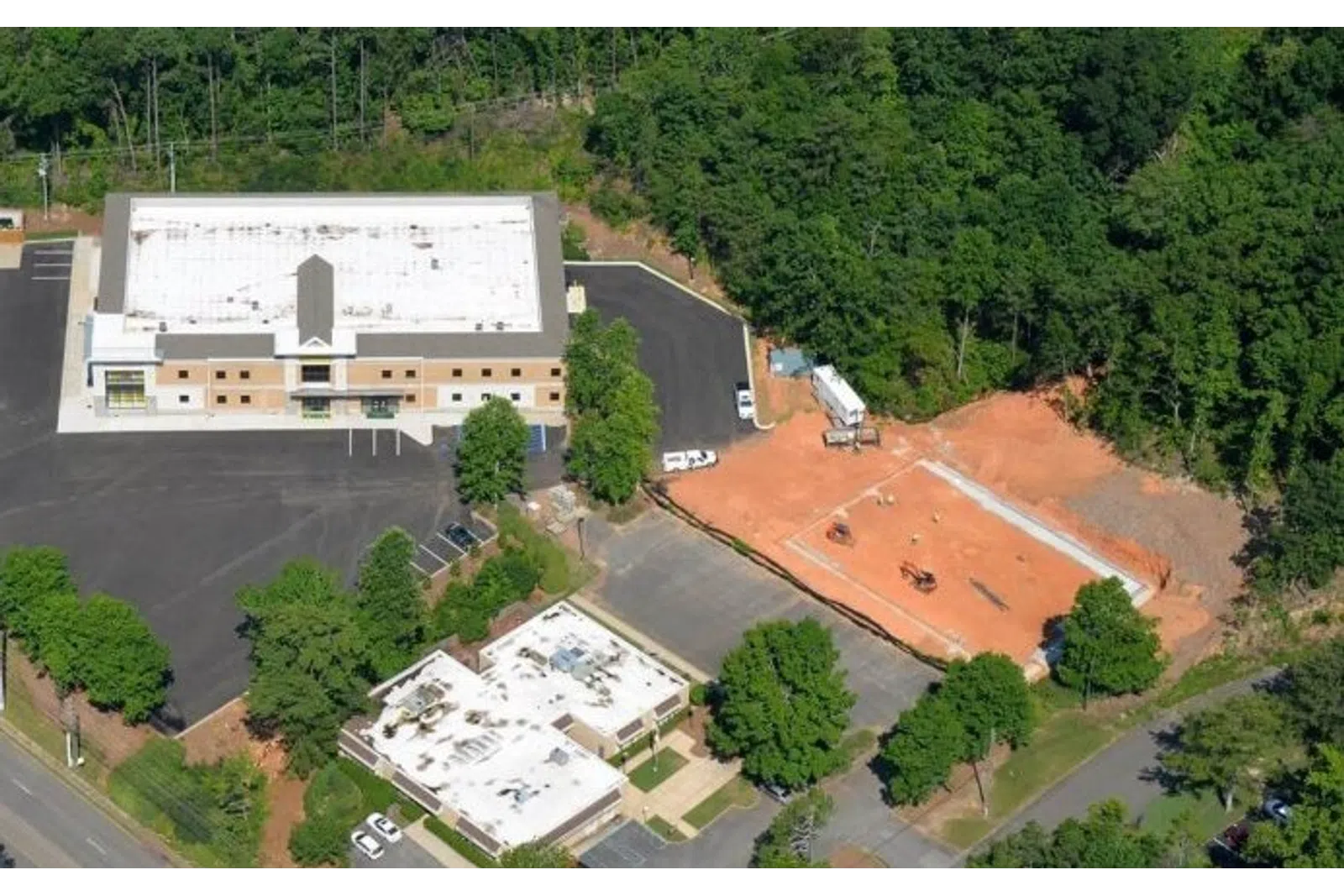 Aerial view of two commercial buildings beside a construction site surrounded by trees and parking lots.